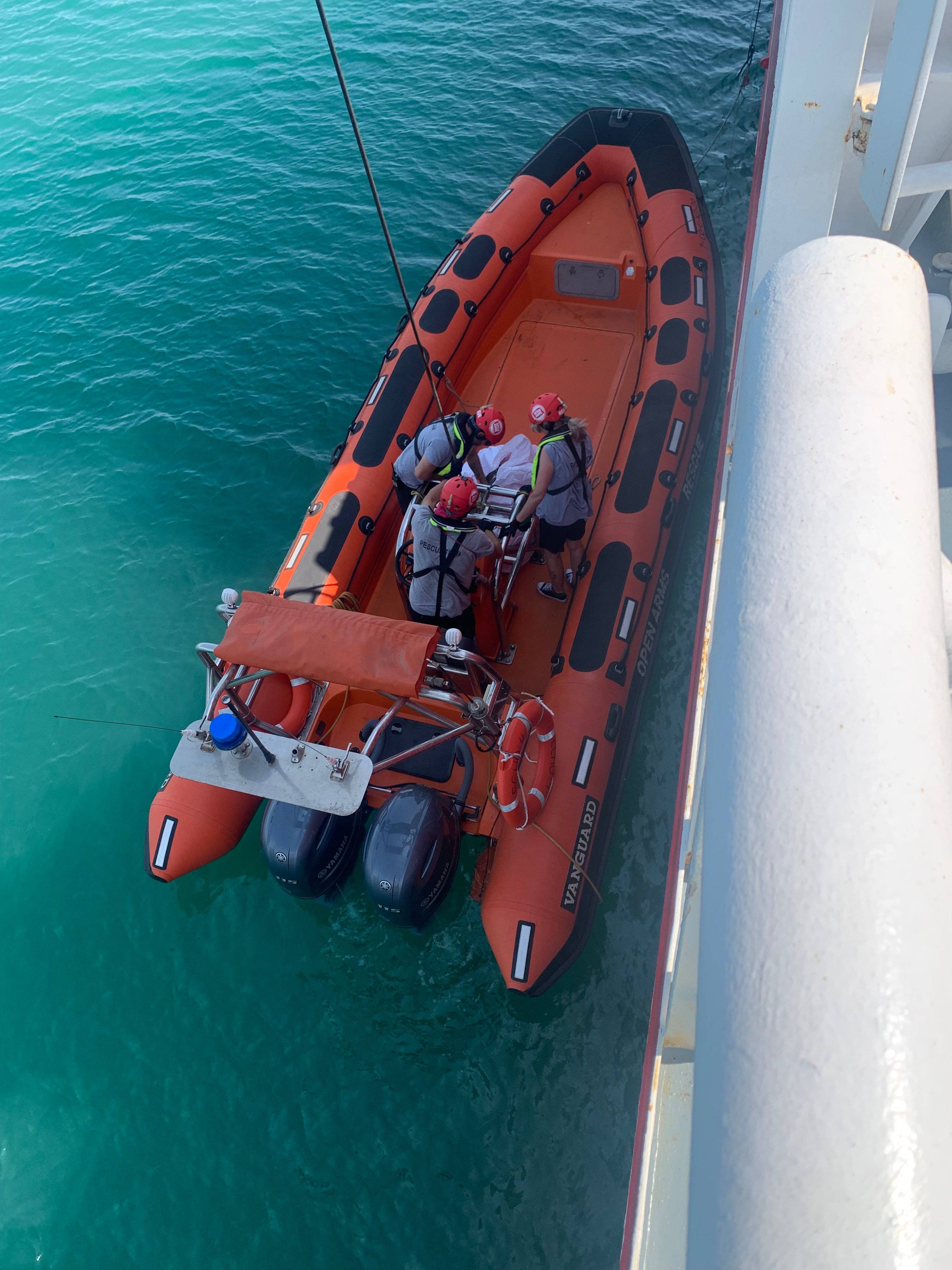 czerwony ponton ratowniczy opuszczony na wodę przy burcie statku. W środku ratownicy przygotowują ratowaną osobę do wciągnięcia na pokład