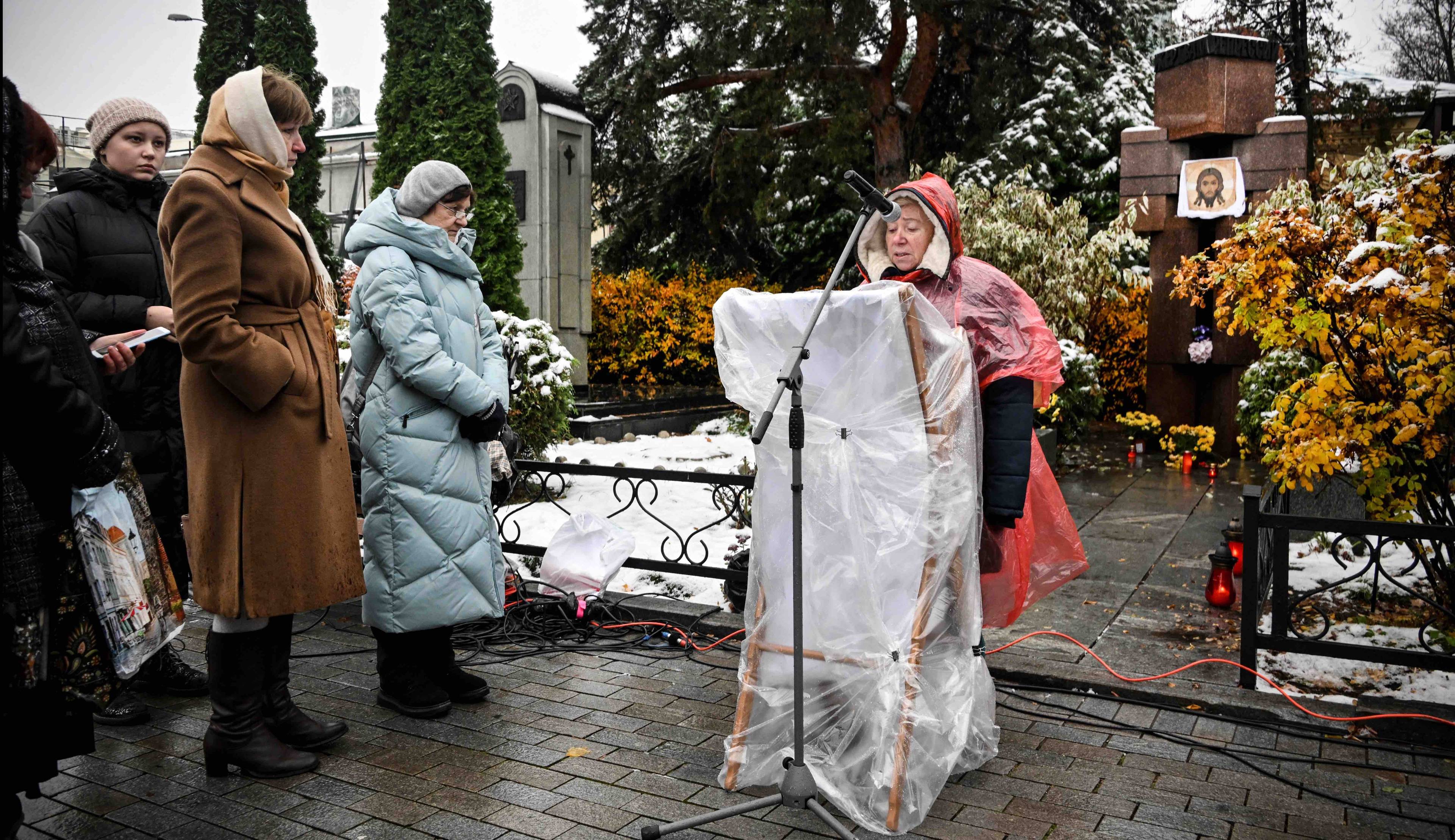 Aktywiści stoją przed pomnikiem na cmentarzu w Moskwie, kobieta stojąca przed mównicą odczytuje listę nazwisk ofiar reżimu stalinowskiego. Memoriał
