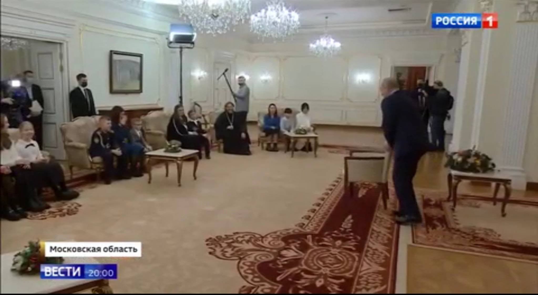 Putin siada na krześle. Po drugiej stronie pod świaną na fotelach i kozetkach dzieci z matkami