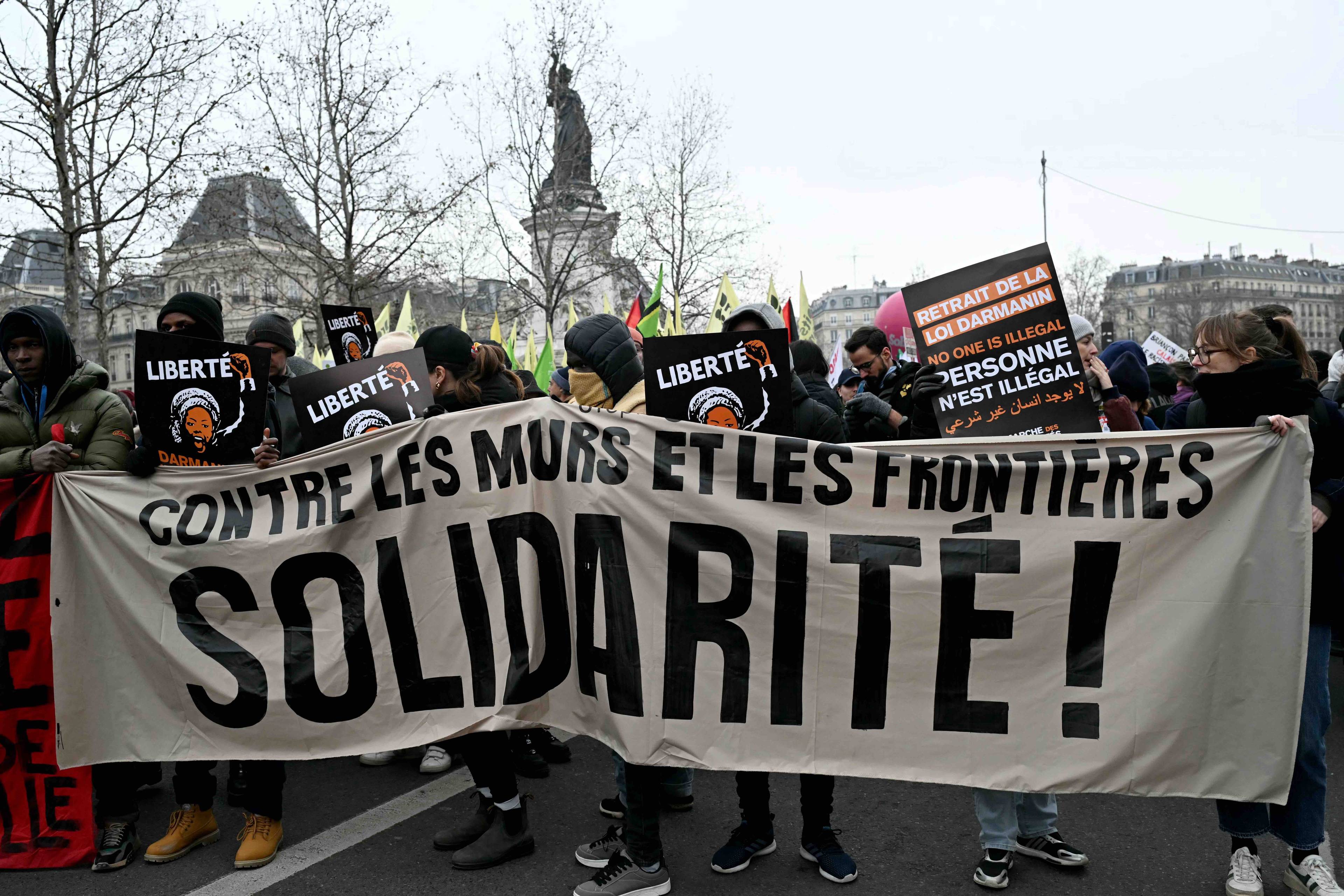 Demonstranci w Paryżu niosą transparent z napisem w języku francuskim {Orzeciw murom i granicom, solidarność”. Nowe prawo migracyjne, Francja.