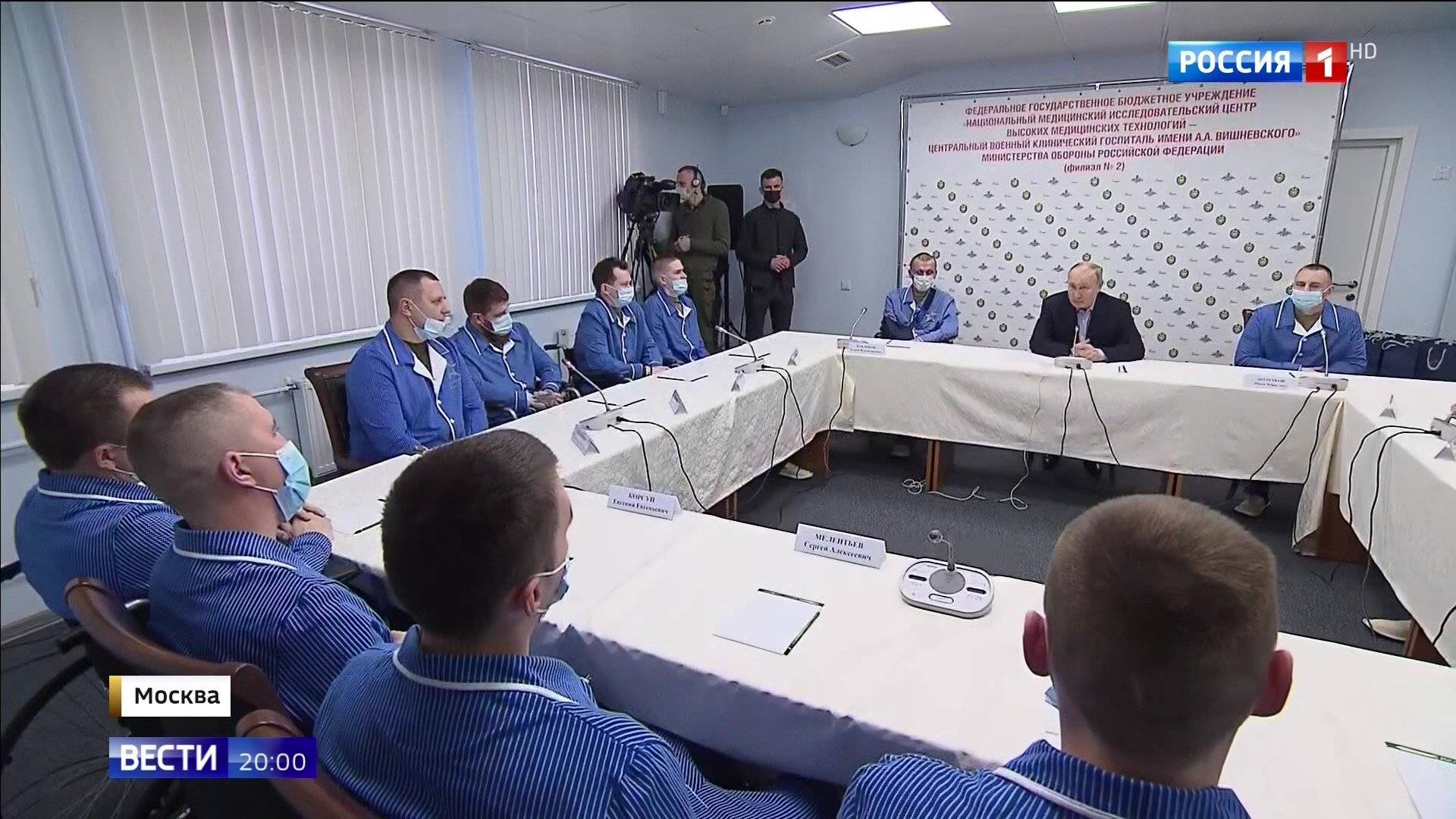 Putin i ranni wojskowi w niebieskich piżamach wokól stołu z białym obrusem