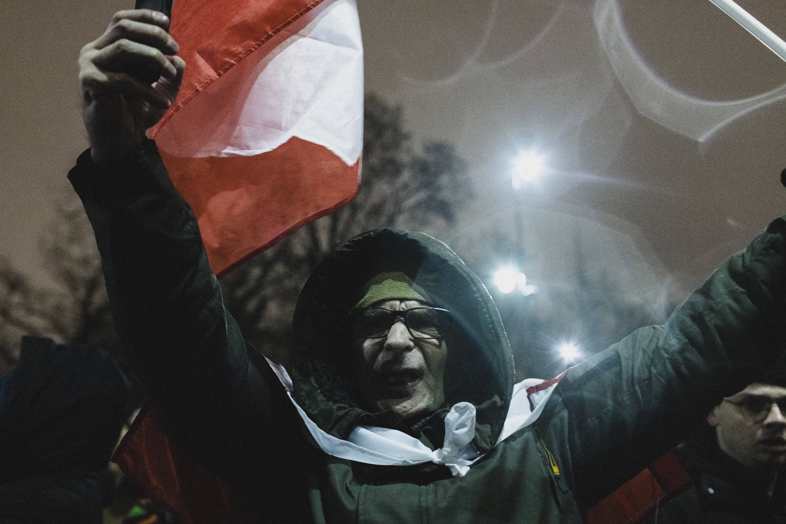 mężczyzna w kapturze powiewający polską flagą