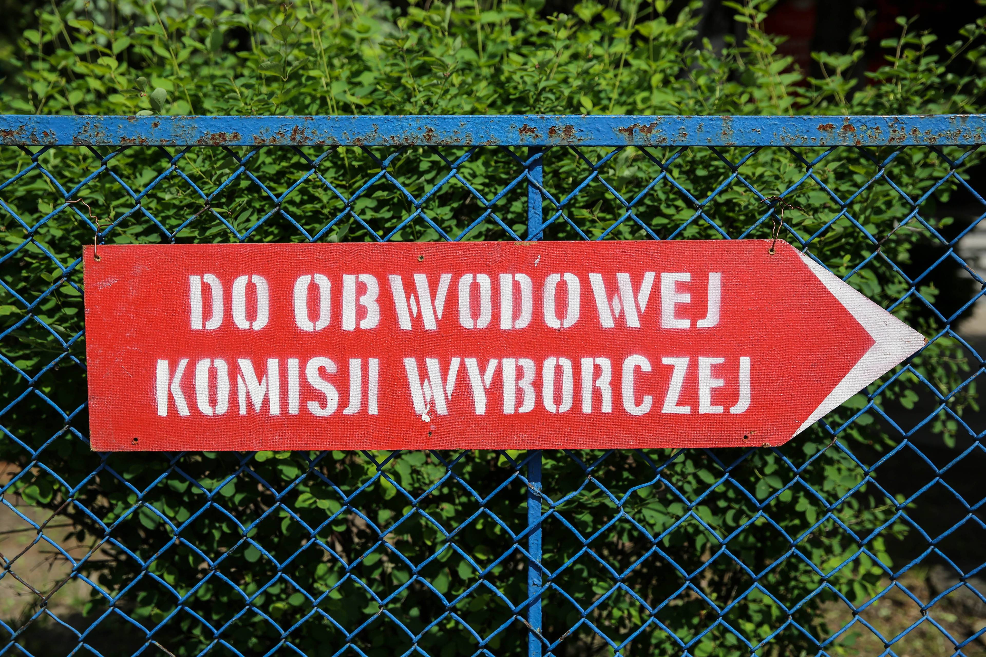 Zdjęcie przedstawia czerwoną tablicę z napisem Do Obwodowej Komisji Wyborczej