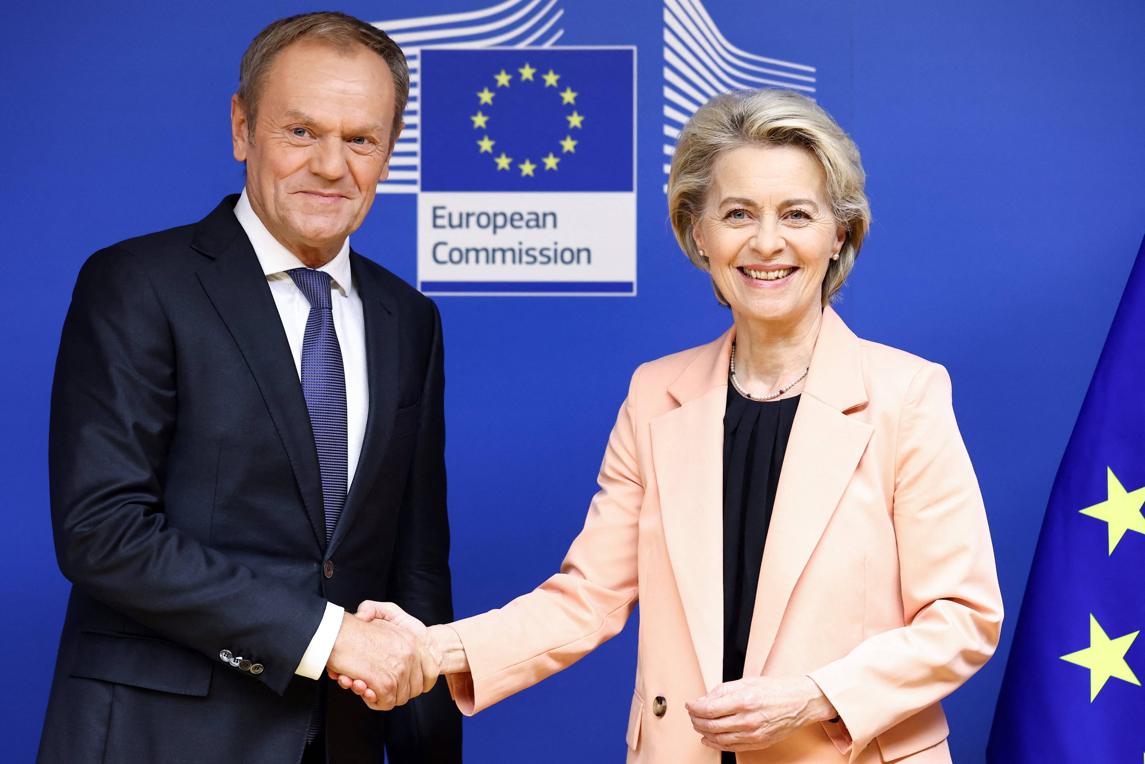 Donald Tusk i szefowa Komisji Europejskiej Ursula von der Leyen podają sobie ręce. Powyżej napis European Commission i unijne gwiazdki