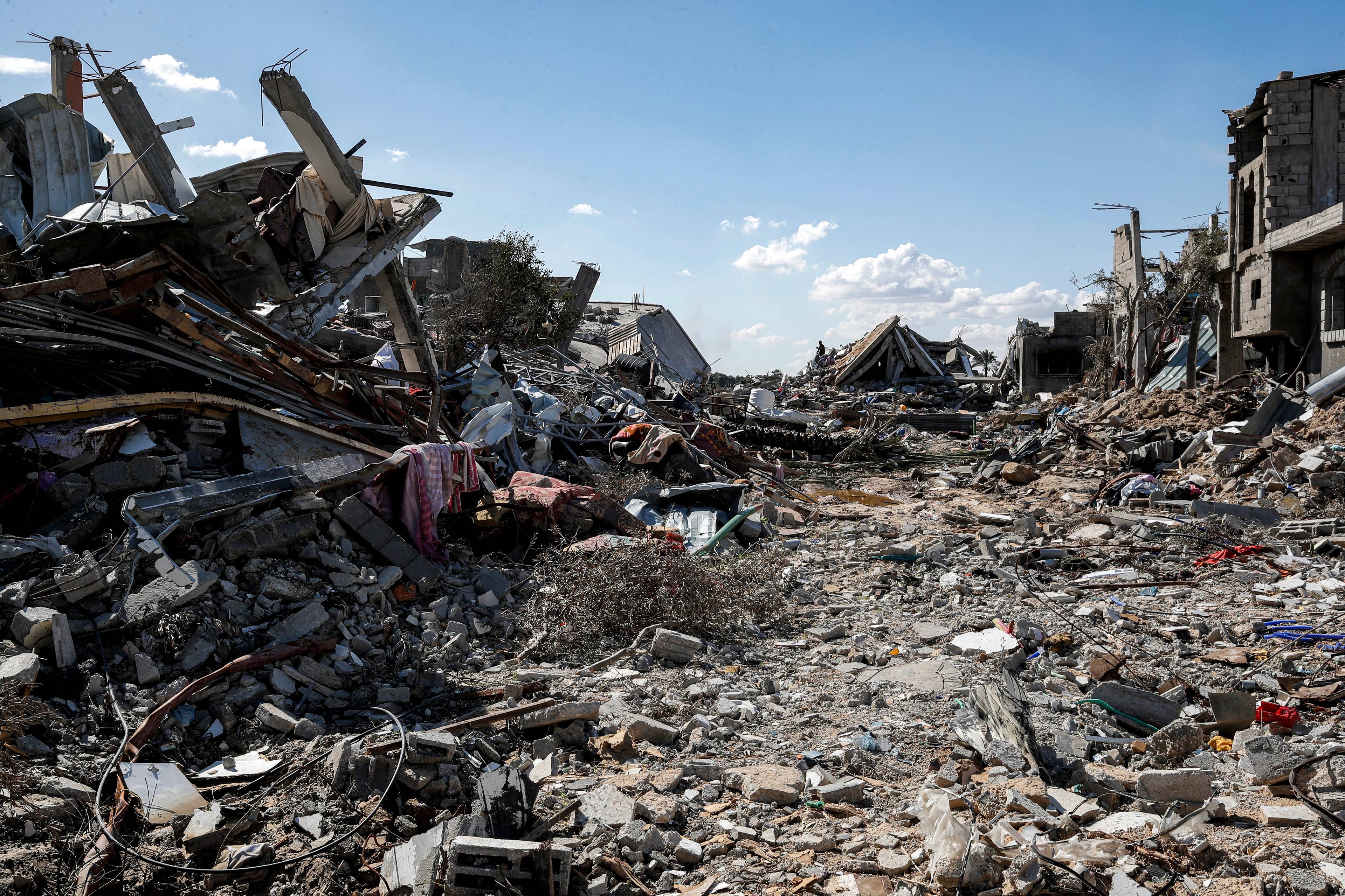 Obraz zniszczeń w Gazie. W tle widać niebieskie niebo, na pierwszym planie kompletnie zniszczona ulica i ruiny budynków z obu stron.