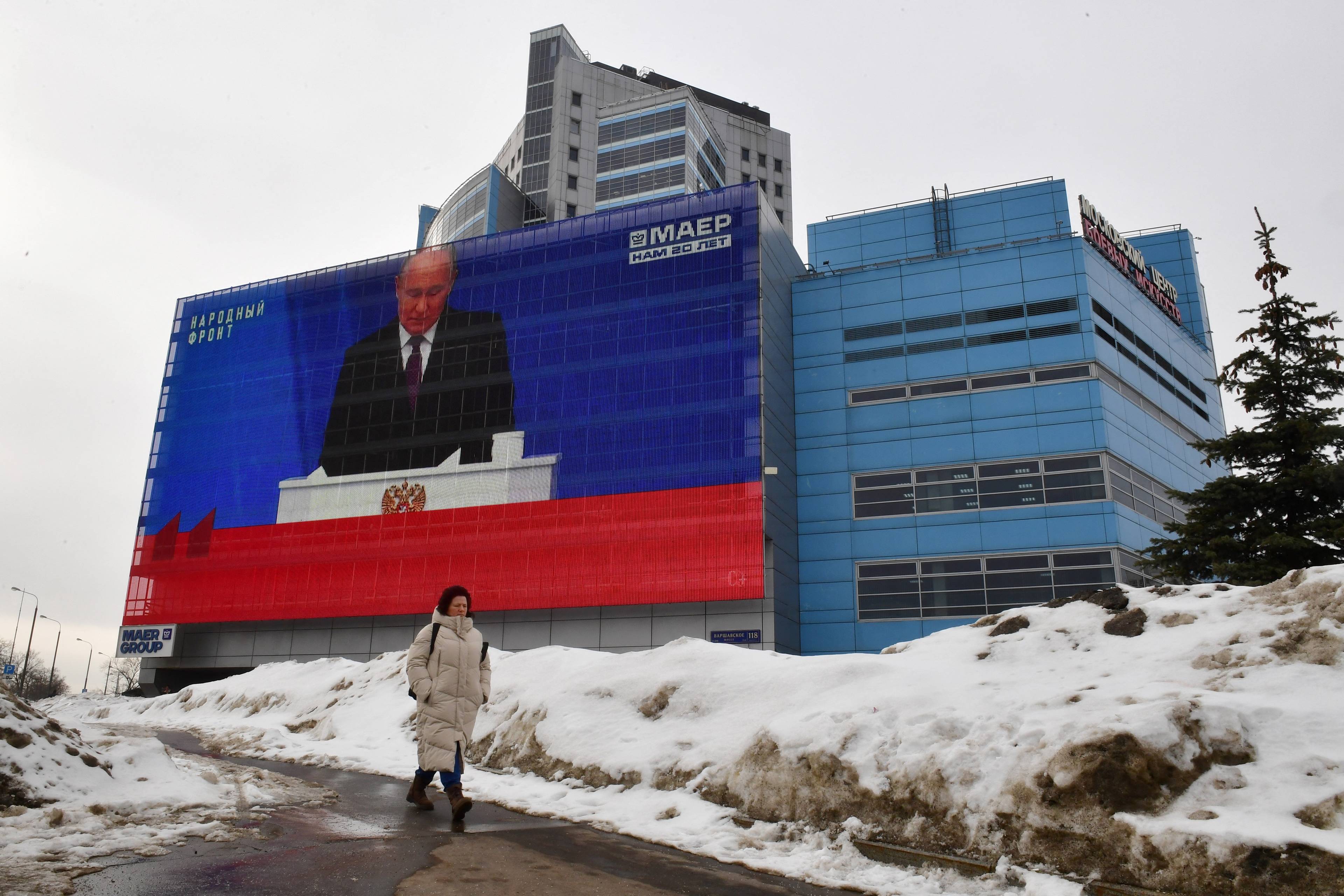 Orędzie Putina wyświetlane na wielkim ekranie na budynku przy zaśnieżonej ulicy, kobieta, która idzie odwrócona do tego plecami