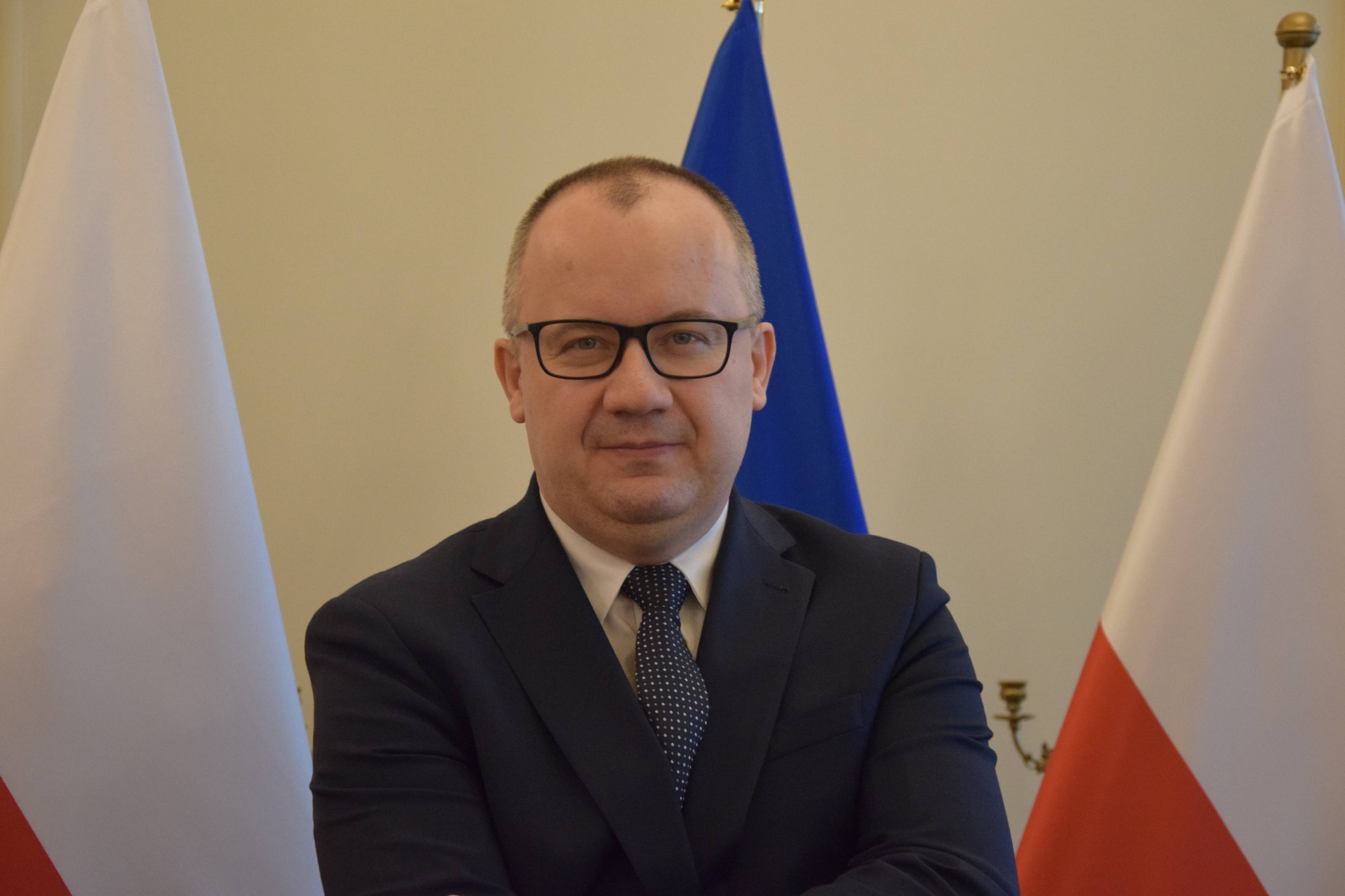Adam Bodnar pozuje do zdjęcia na tle flag polskiej i UE