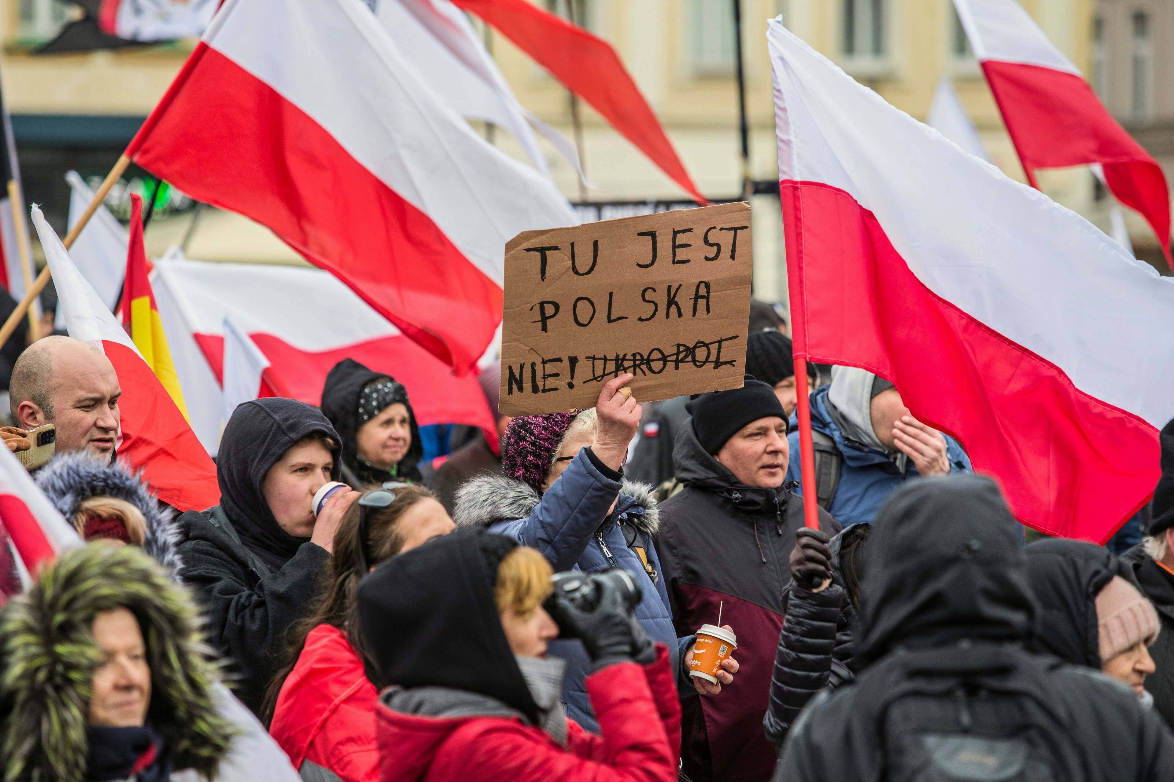 Manifestacja przeciwko Ukraińcom w Polsce, wśród polskich flag osoba stoi z transparentem: "Tu jest Polska, nie Ukropol"