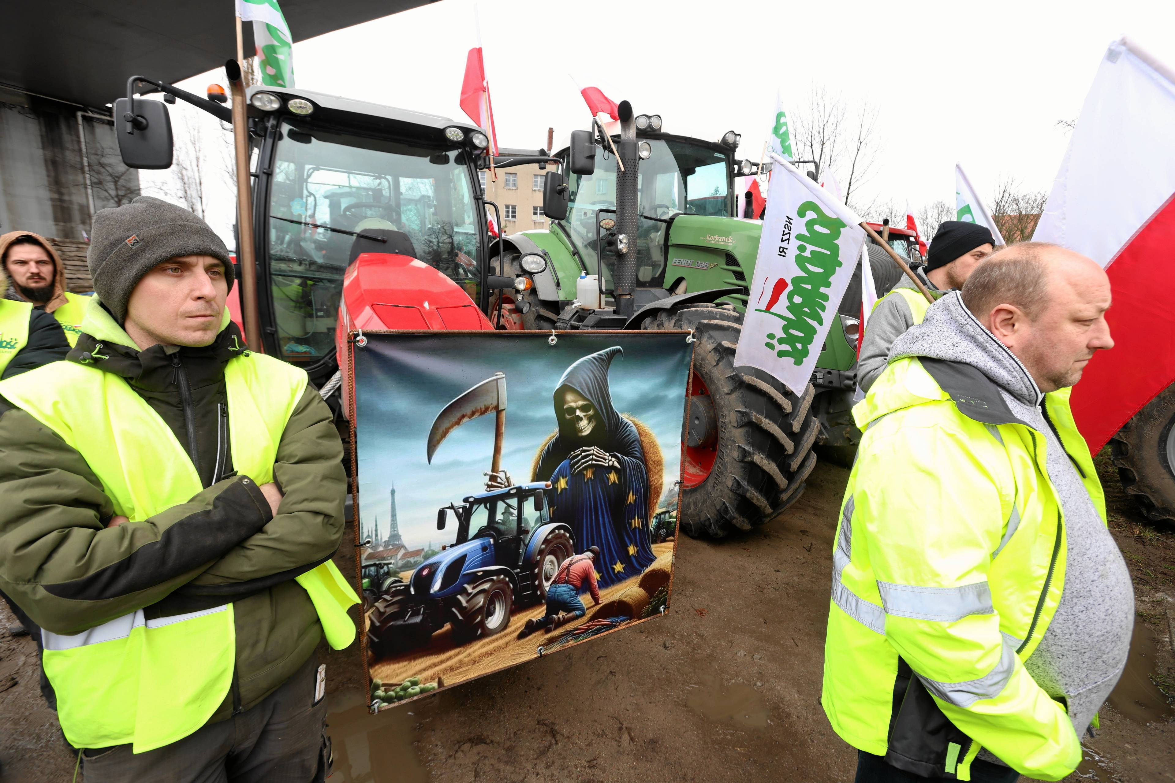 Protestujący rolnicy trzymają obrazek, na którym Unia Europejska przedstawiona jest jako śmierć z kosą