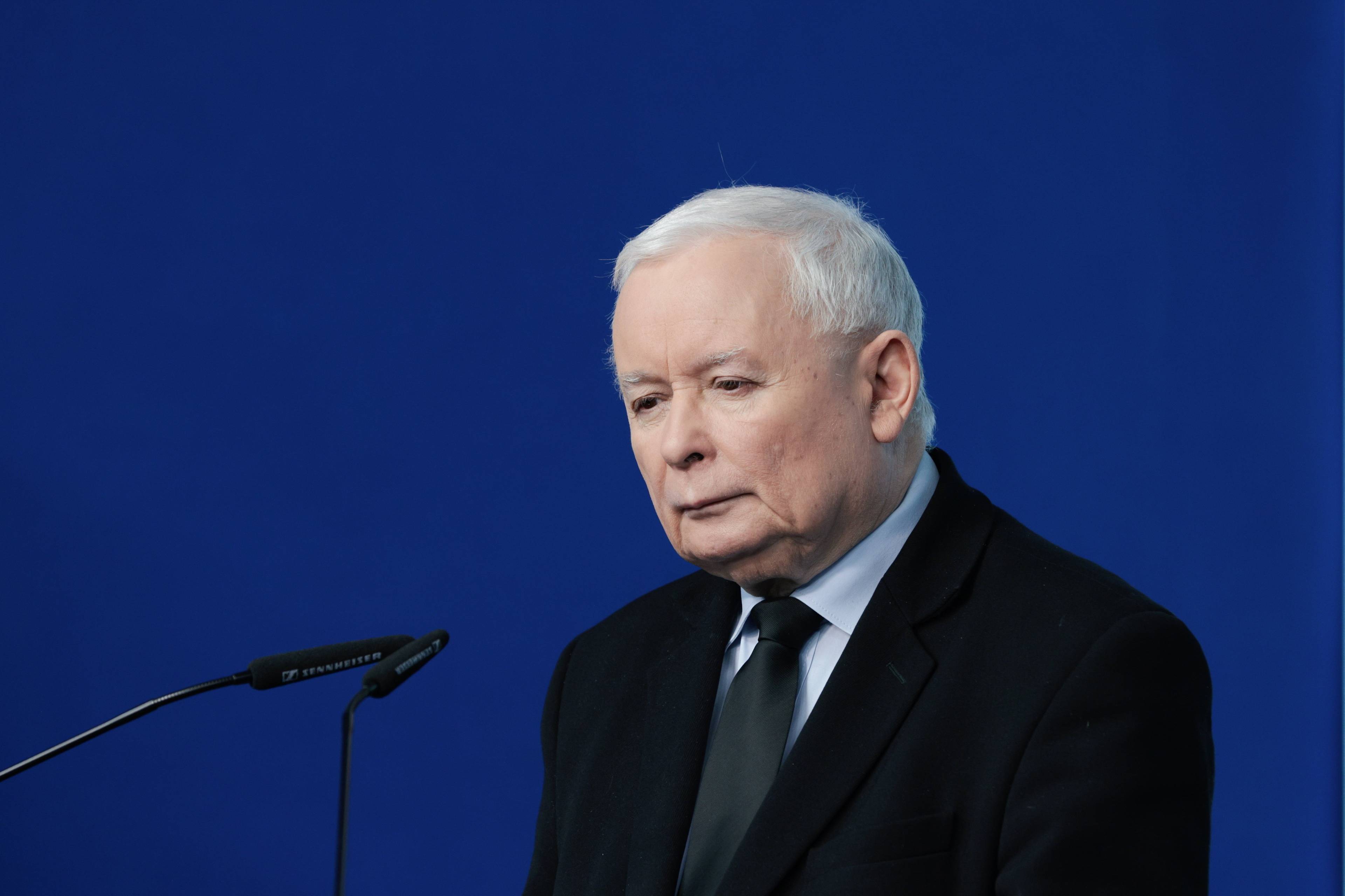 Jarosław Kaczyński przed mikrofonem na niebieskim tle