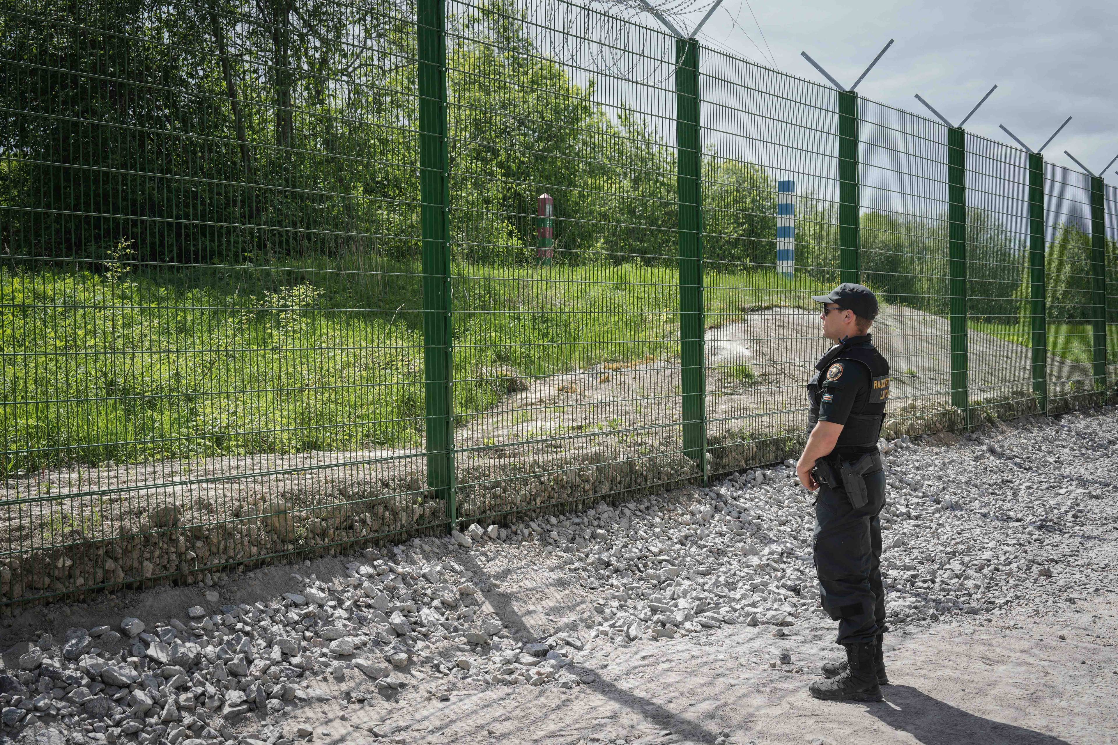 Metalowy płot zakończony drutem kolczastym na granicy fińsko-rosyjskiej, przed płotem stoi strażnik graniczny. Wojny hybrydowe