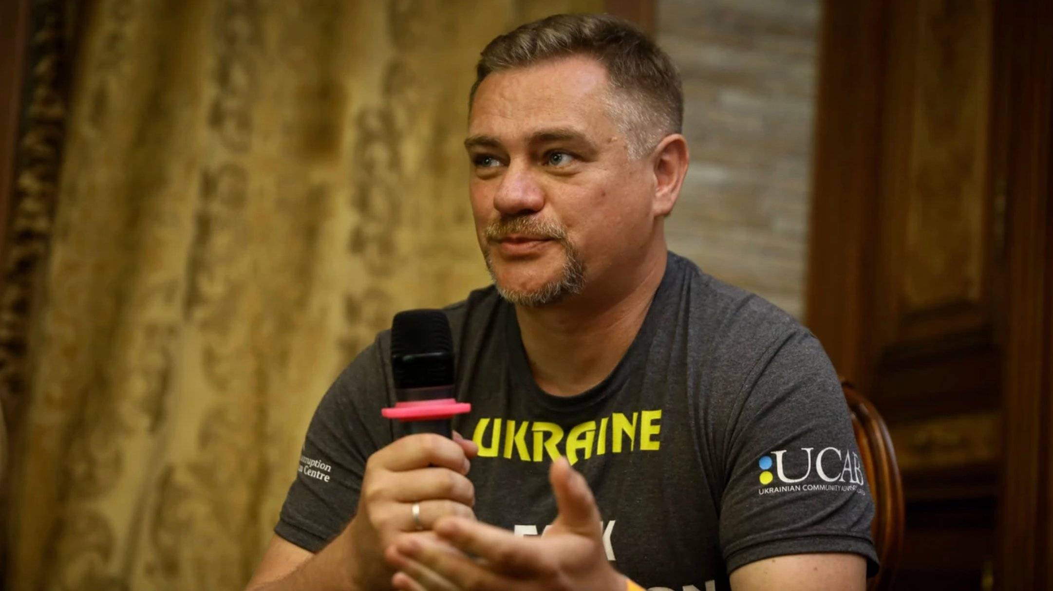 Dziennikarz Jurij Nikołow w tiszercie z napisem Ukraina mówi do mikrofonu. Dziennikarze śledczy