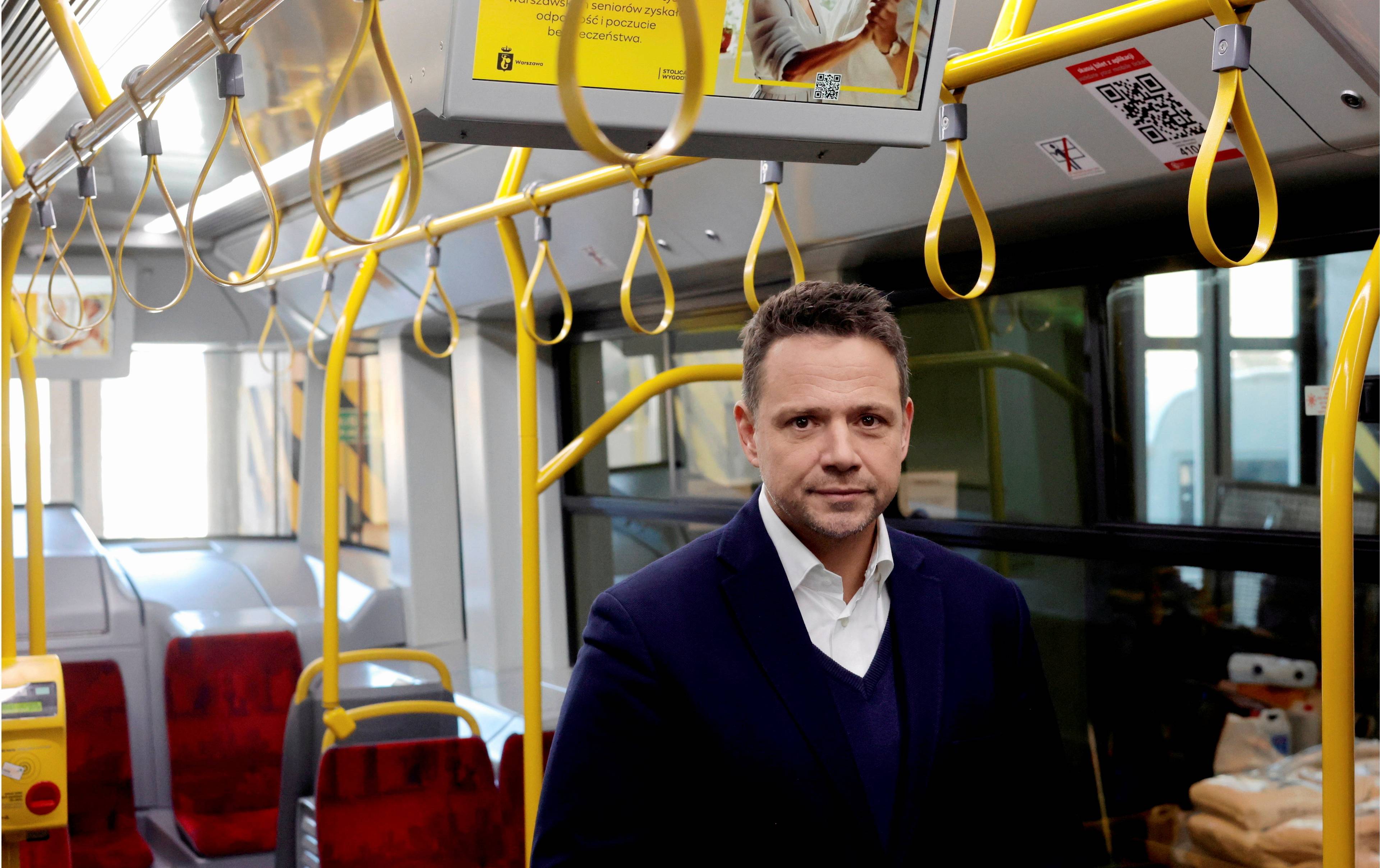 Rafał Trzaskowski stoi w tramwaju. Nad głową ma żółte uchwyty dla pasażerów