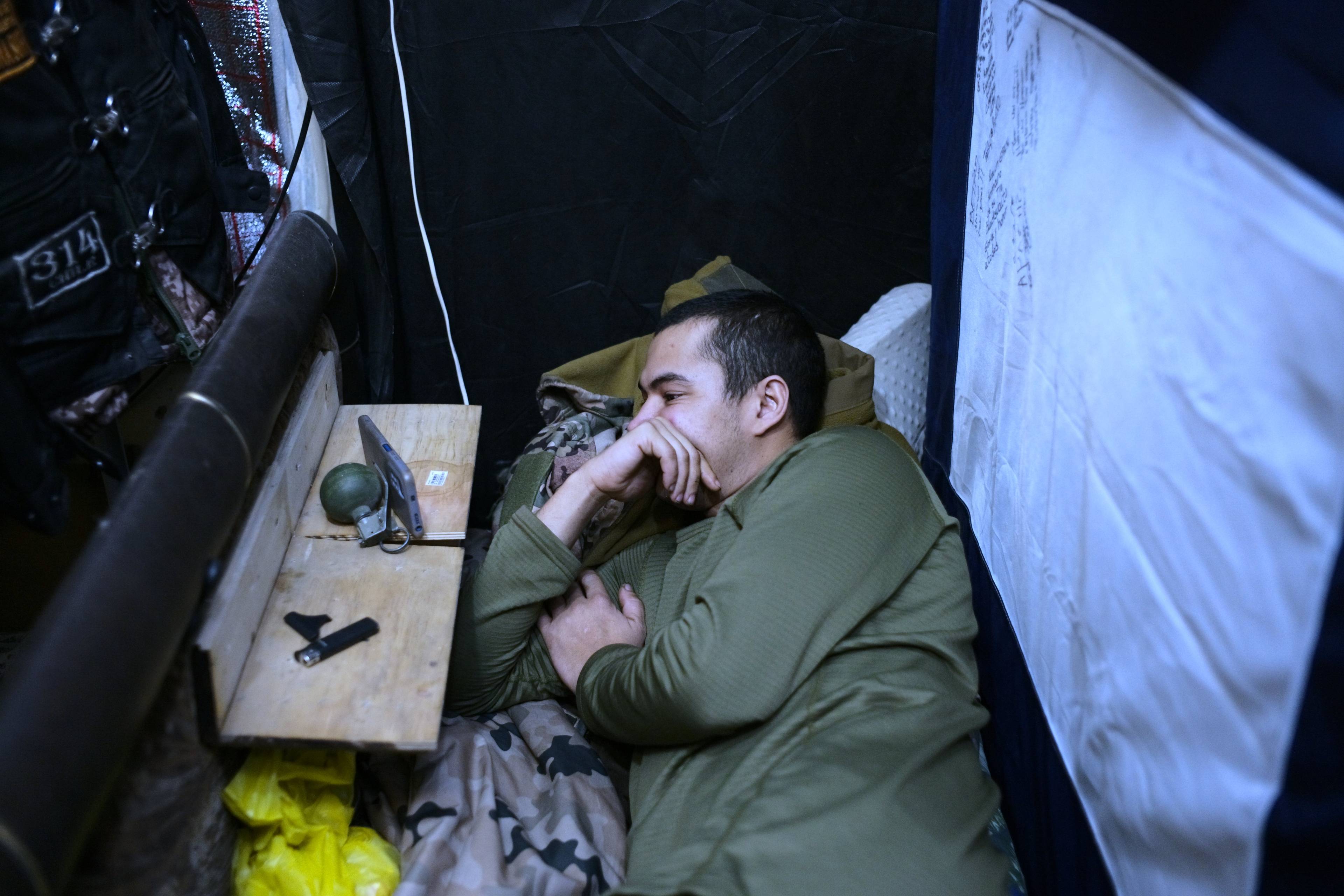 żołnierz leżący na posłaniu patrzący w telefon oparty na granacie