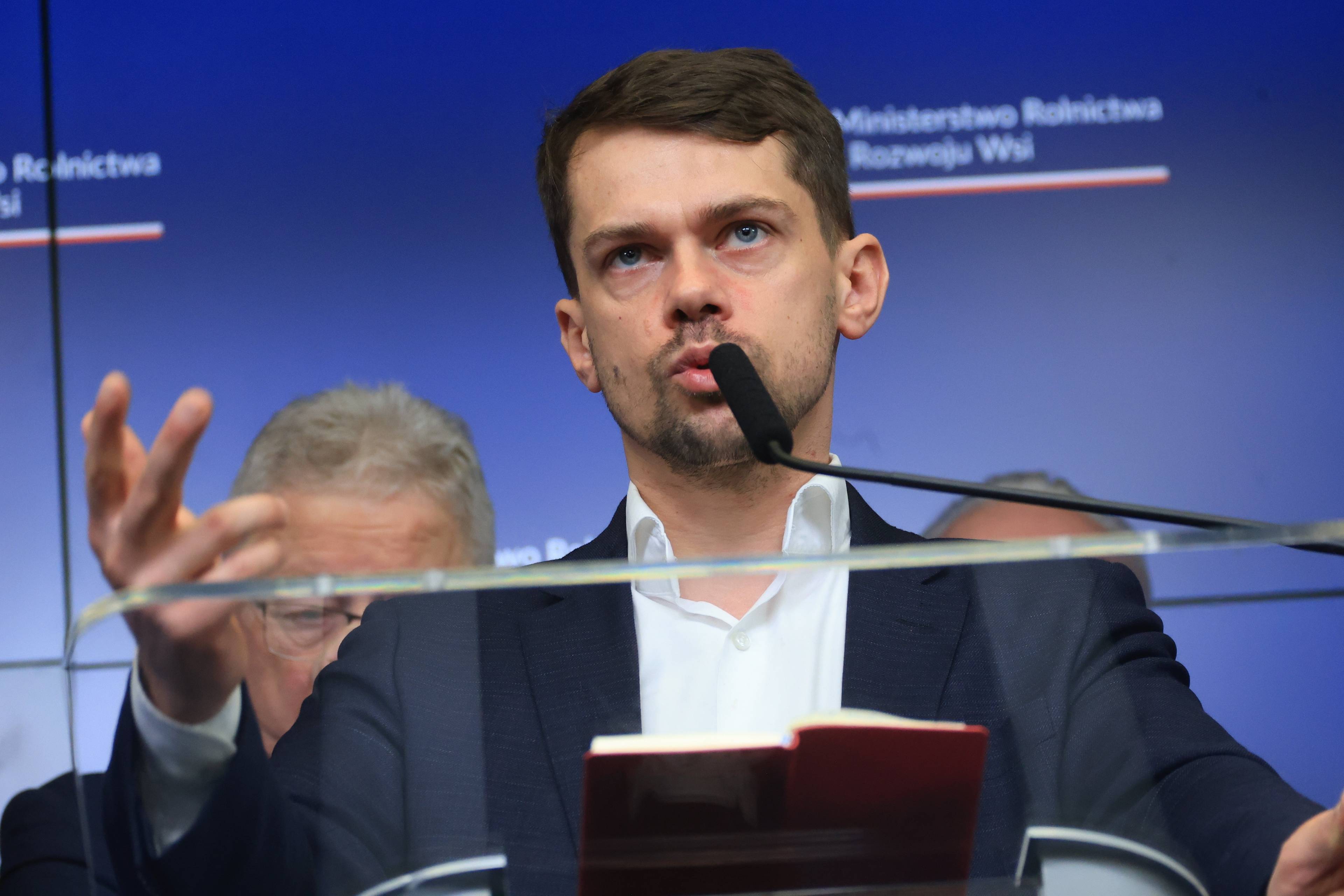 Michał Kołodziejczak, wiceminister rolnictwa z uniesioną dłonią i mikrofonem