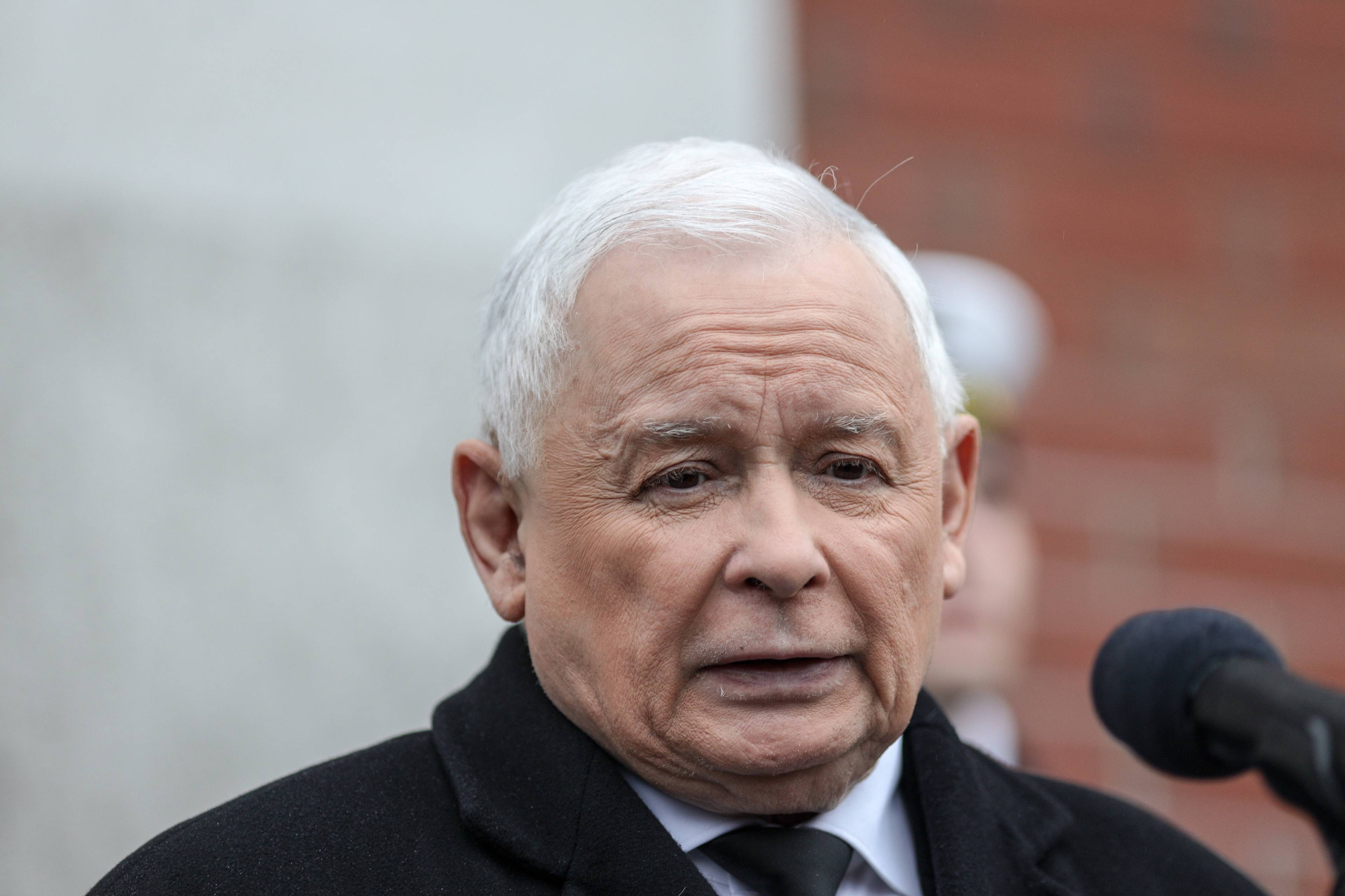 Jarosław Kaczyński z niezadowoloną miną, przed mikrofonem
