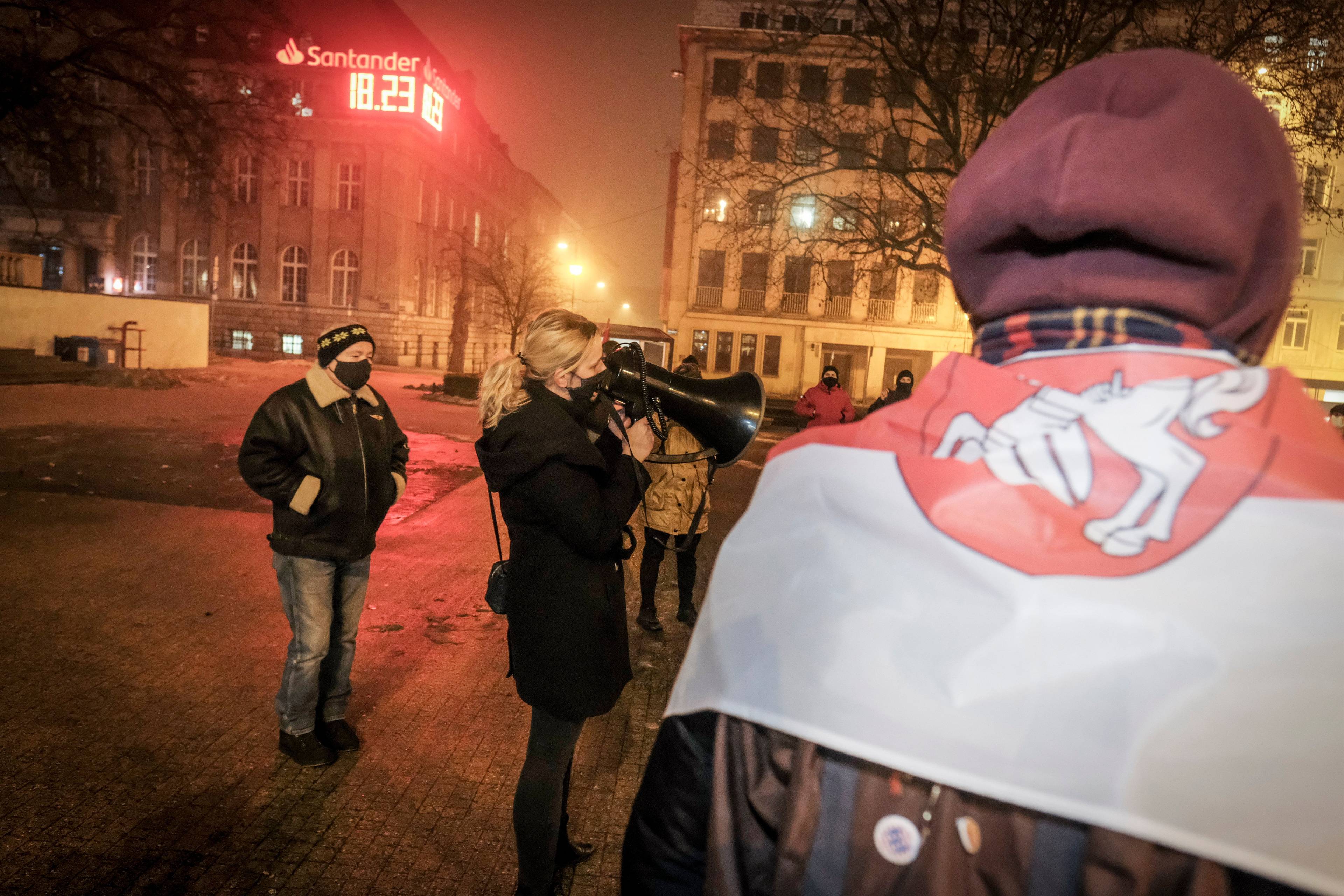 manifestujący z flagą Białorusi (Pogonią) na plecach, w tle ekipa telewizyjna