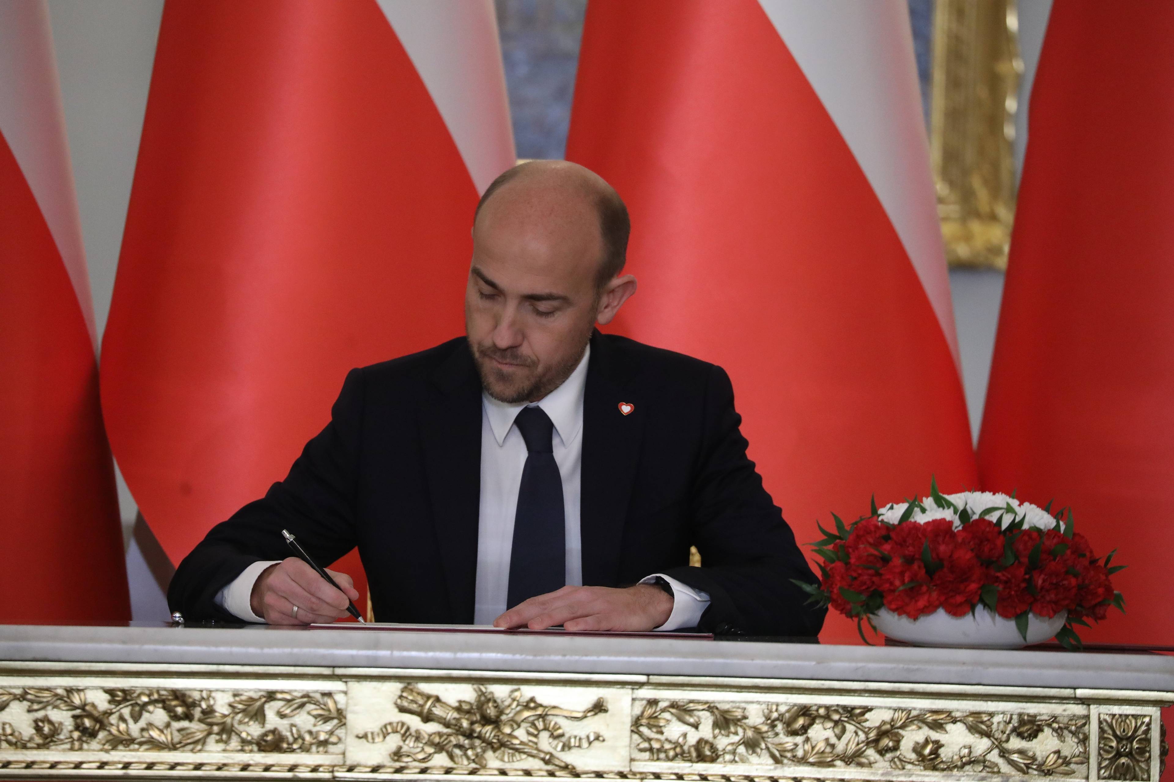 Borys Budka na tle biało-czerwonych flag podpisuje dokument