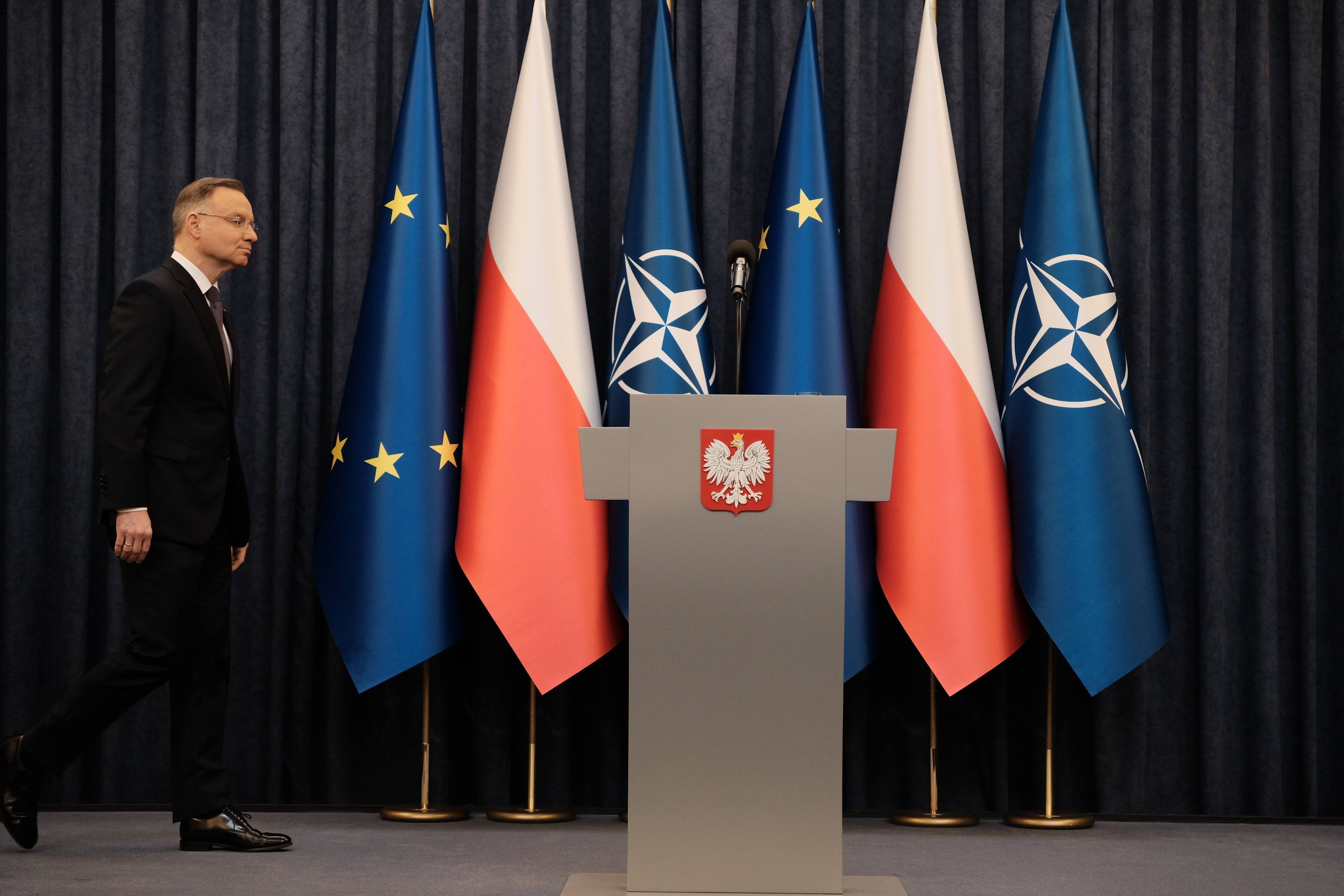 Prezydent Duda wchodzi na podium, na którym stoi szara mównica z godłem Polski