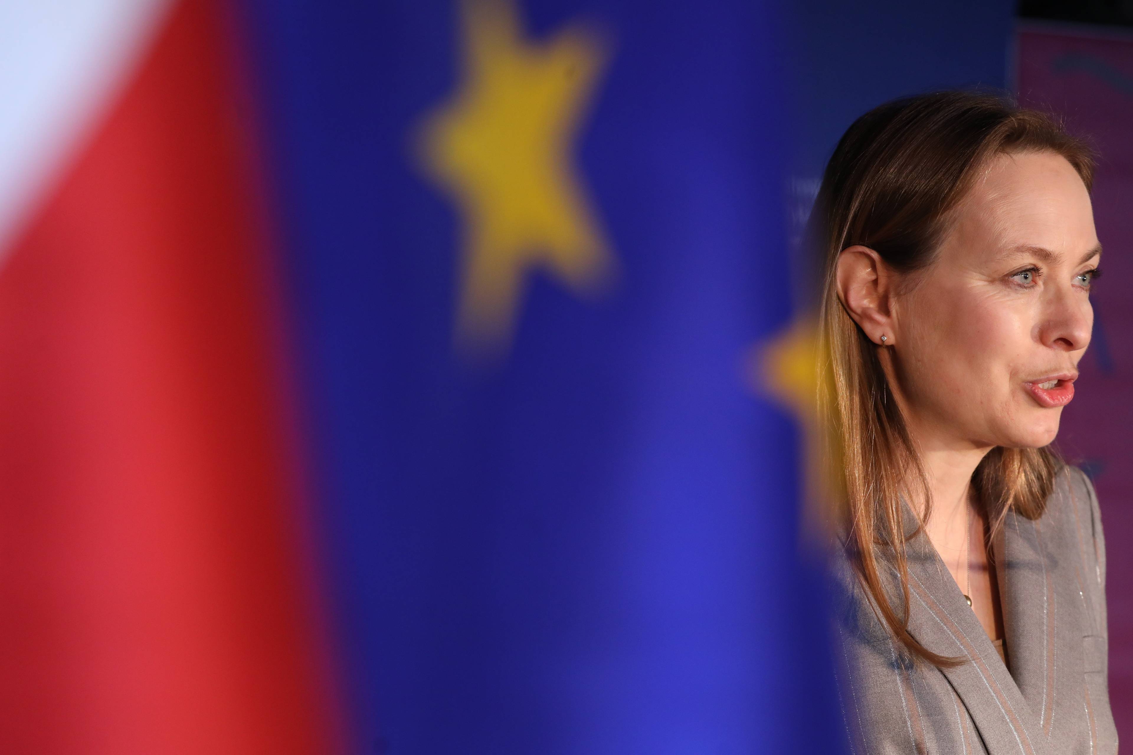 Kobieta w jasnym żakiecie na tle flag UE i Polski