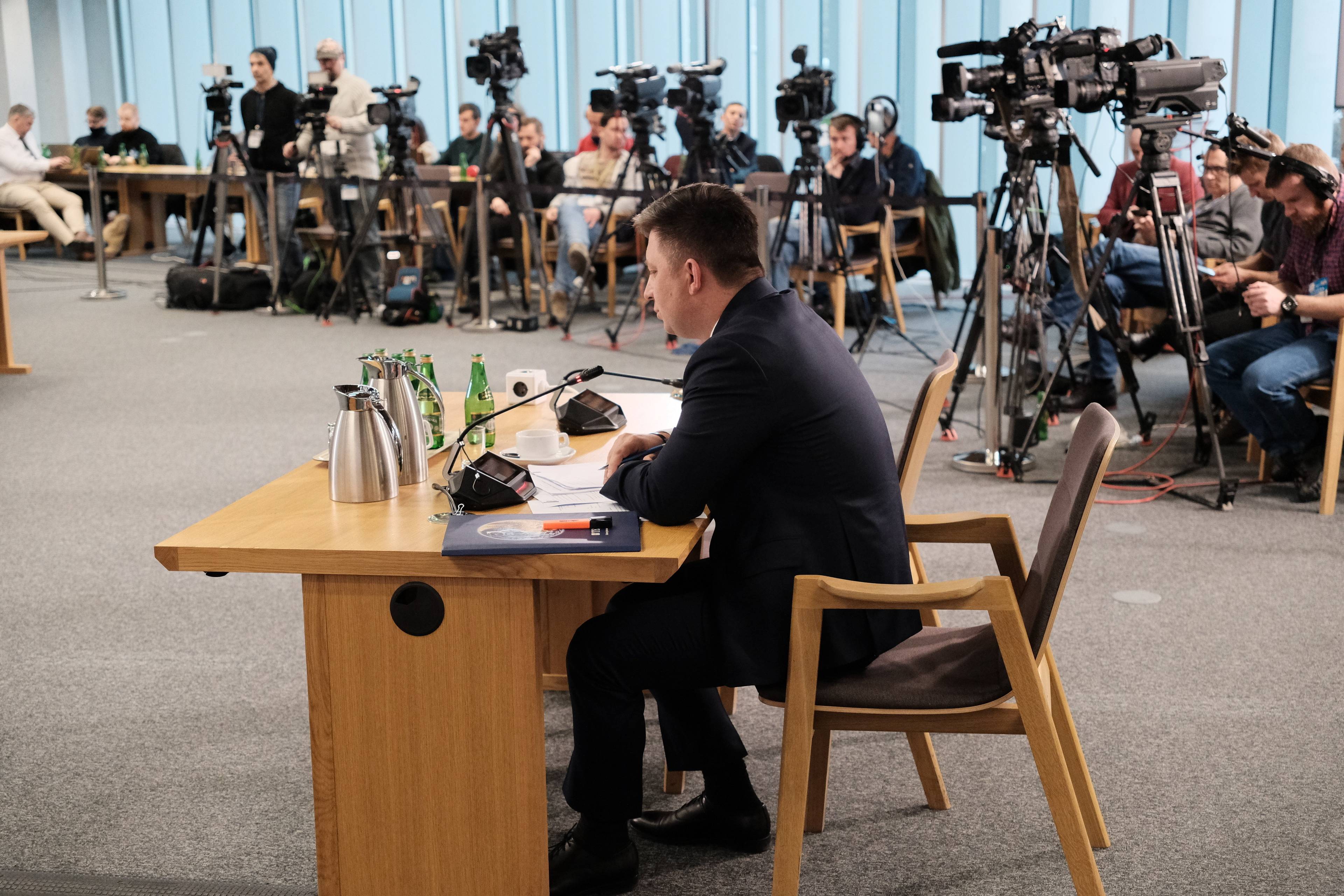 Michał Dworczyk podczas przesłuchania przez sejmową komisję śledczą ds. wyborów kopertowych. Dworczyk w centrum kadru, siedzi przy biurku. W tle rząd kamer telewizyjnych.