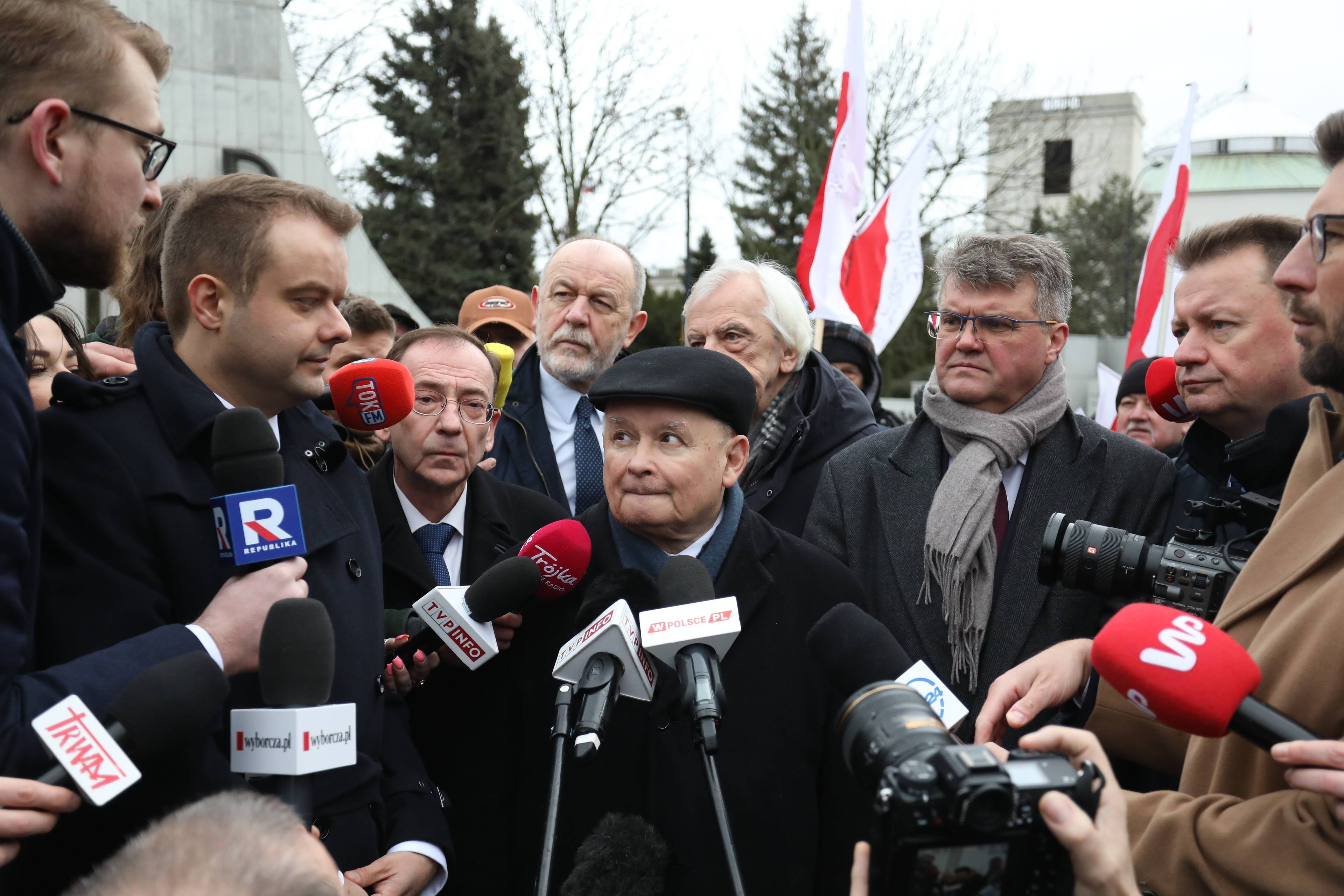 Prezes PiS Jarosław Kaczyński w otoczeniu dziennikarzy oraz Macieja Wąsika i Mariusza Kamińskiego. W tle budynek Sejmu