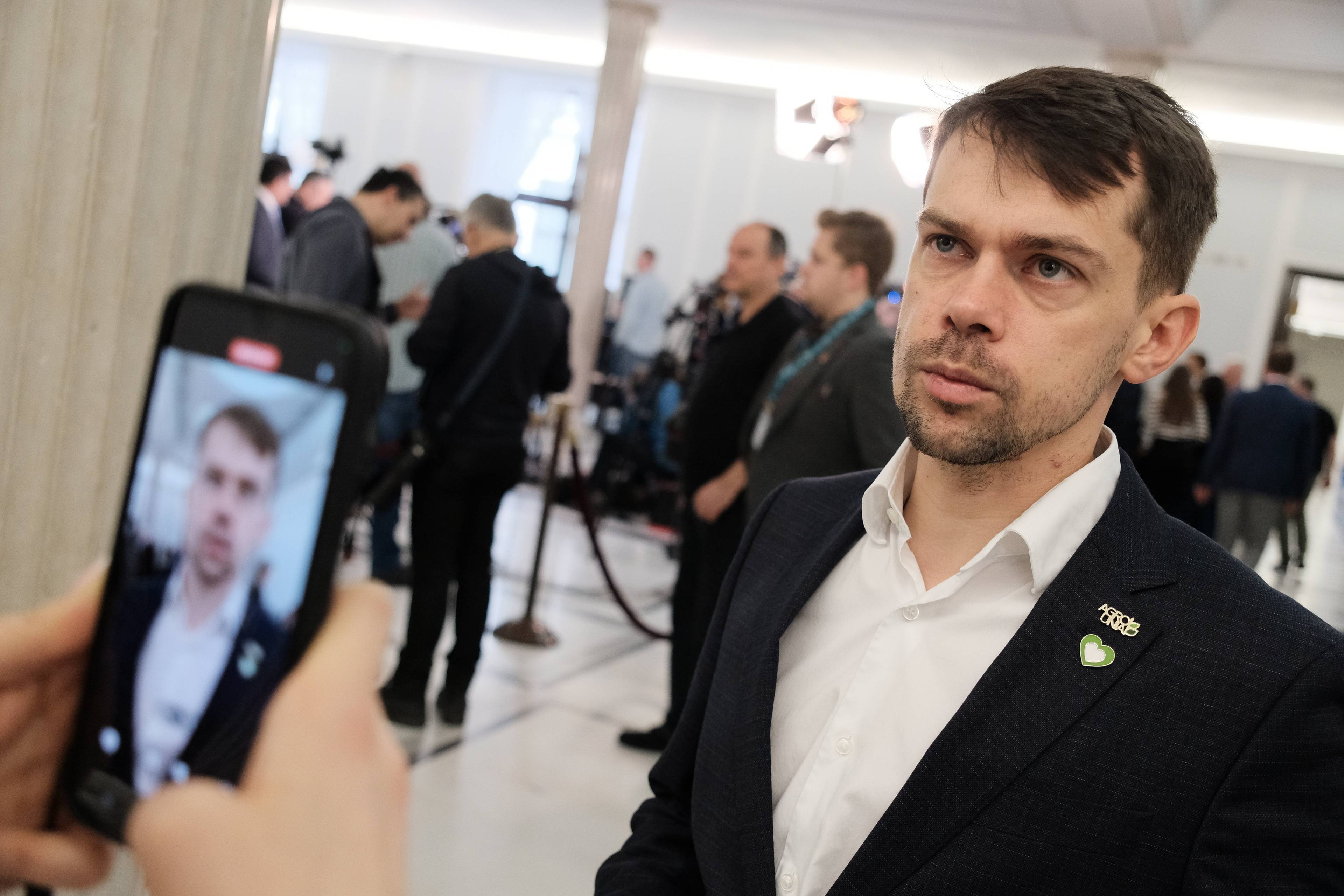 Michał Kołodziejczak w Sejmie. Na pierwszym planie dłonie trzymające telefon komórkowy, którym ktoś nagrywa Kołodziejczaka