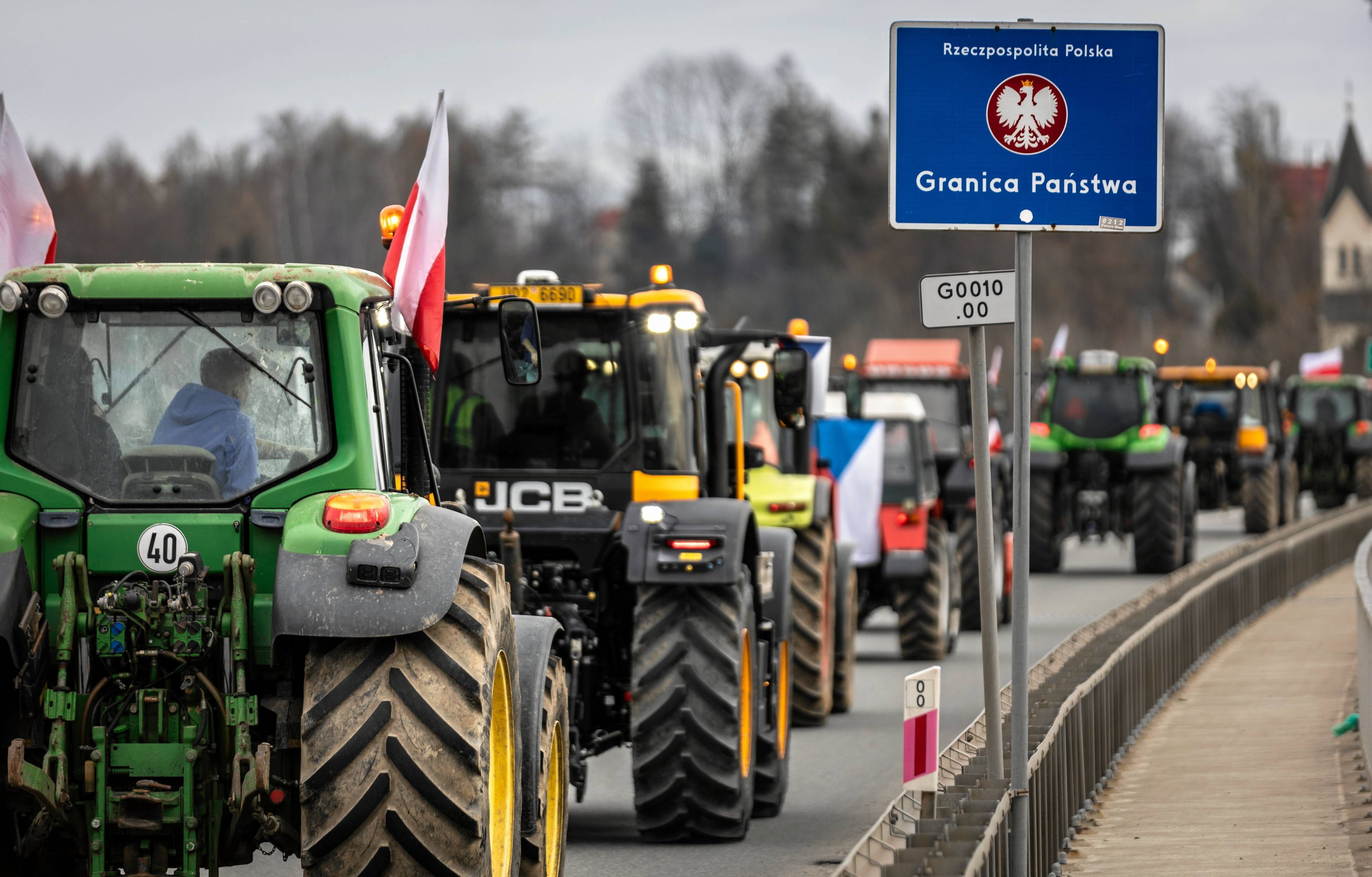 Traktory ustawione jeden za drugim na jezdni, przy drodze znak "granica państwa".