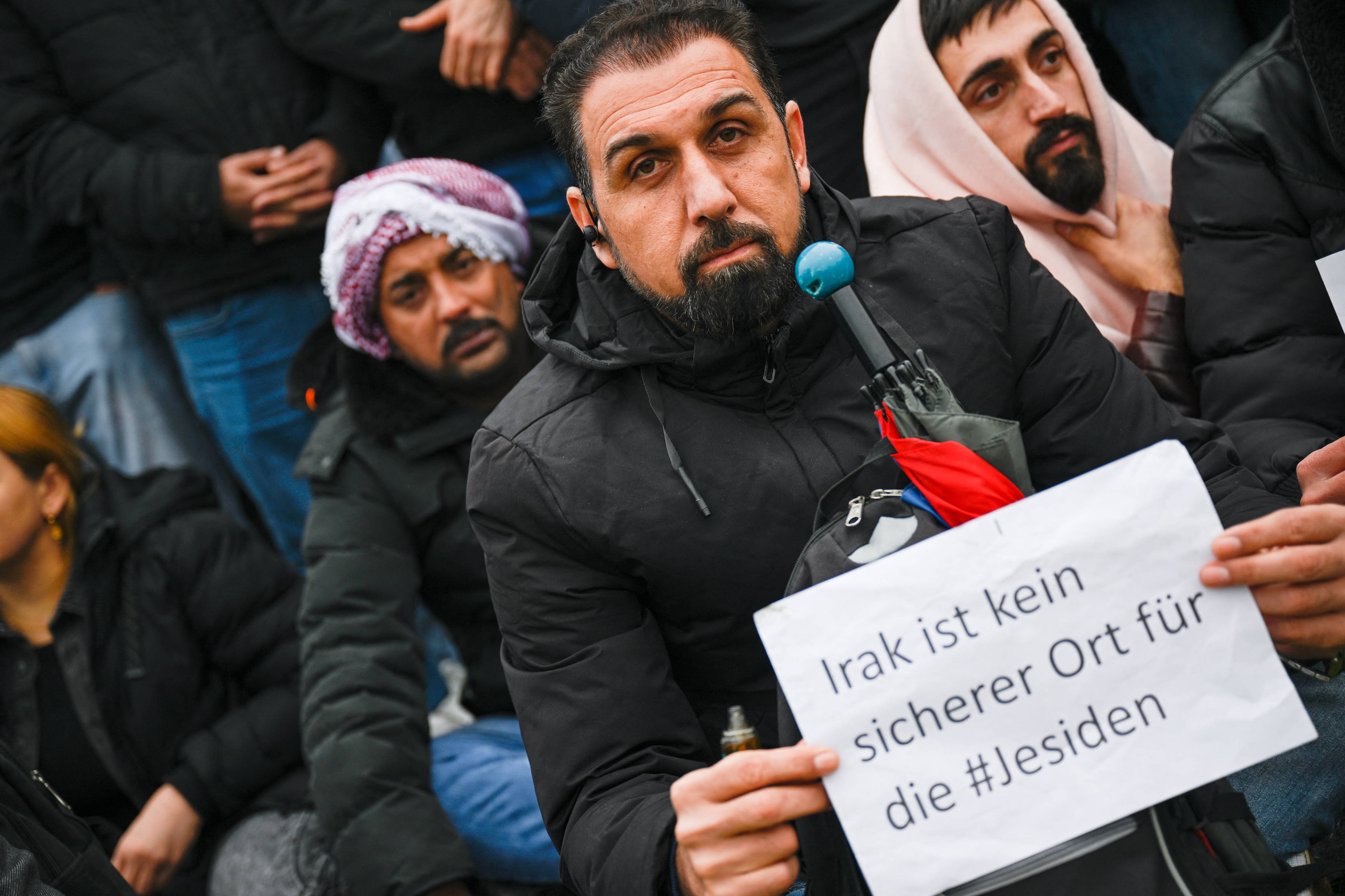 mężczyźni o bliskowschodnich rysach z transparentem po niemiecku: Irak nie jest bezpiecznym krajem dla jezydów