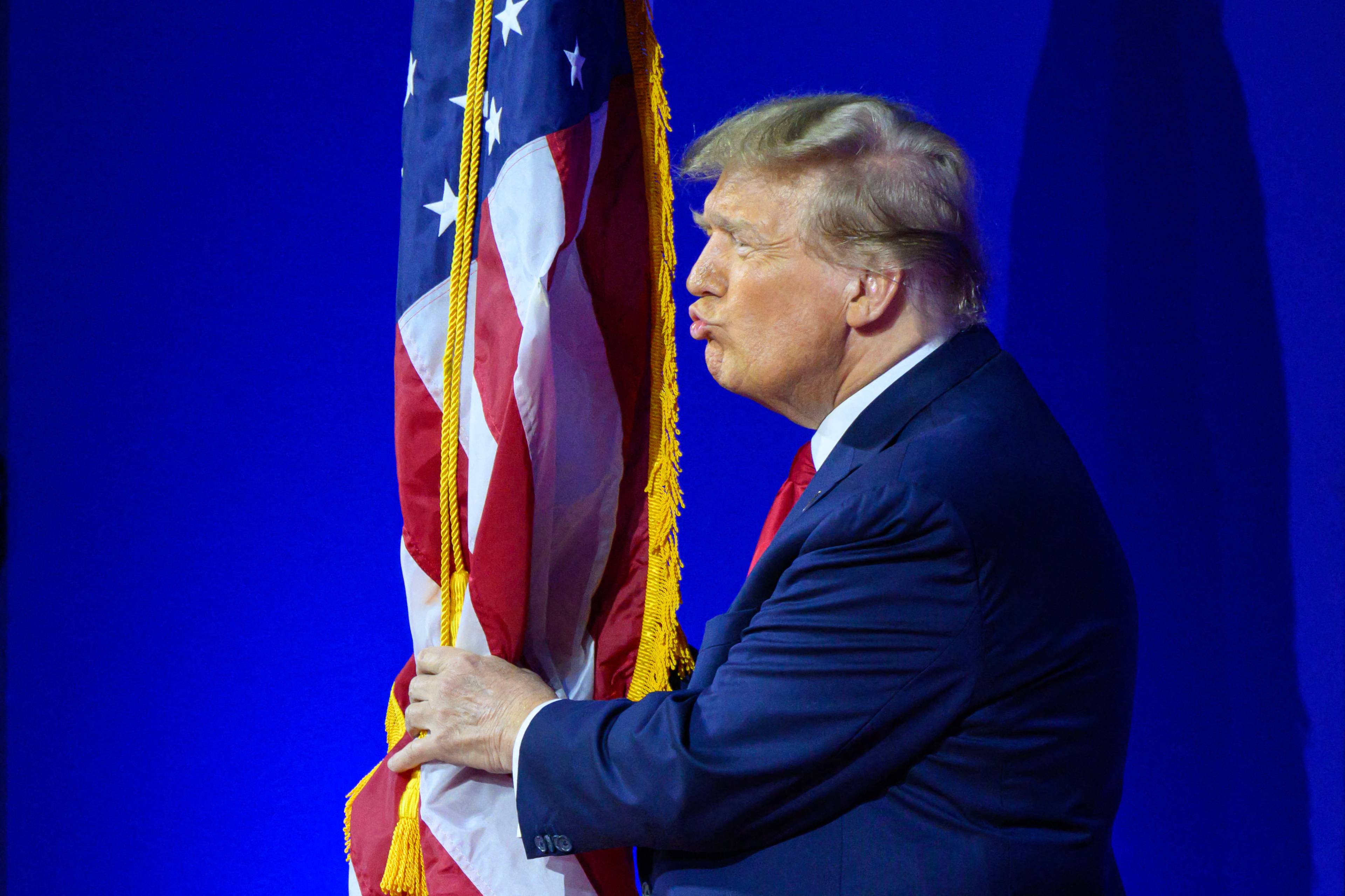 Donald Trump układa usta w dziubek, całując amerykańską flagę