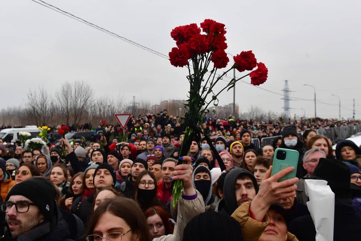 Tłum ludzi, na pierwszym planie uniesione w górę czerwone kwiaty
