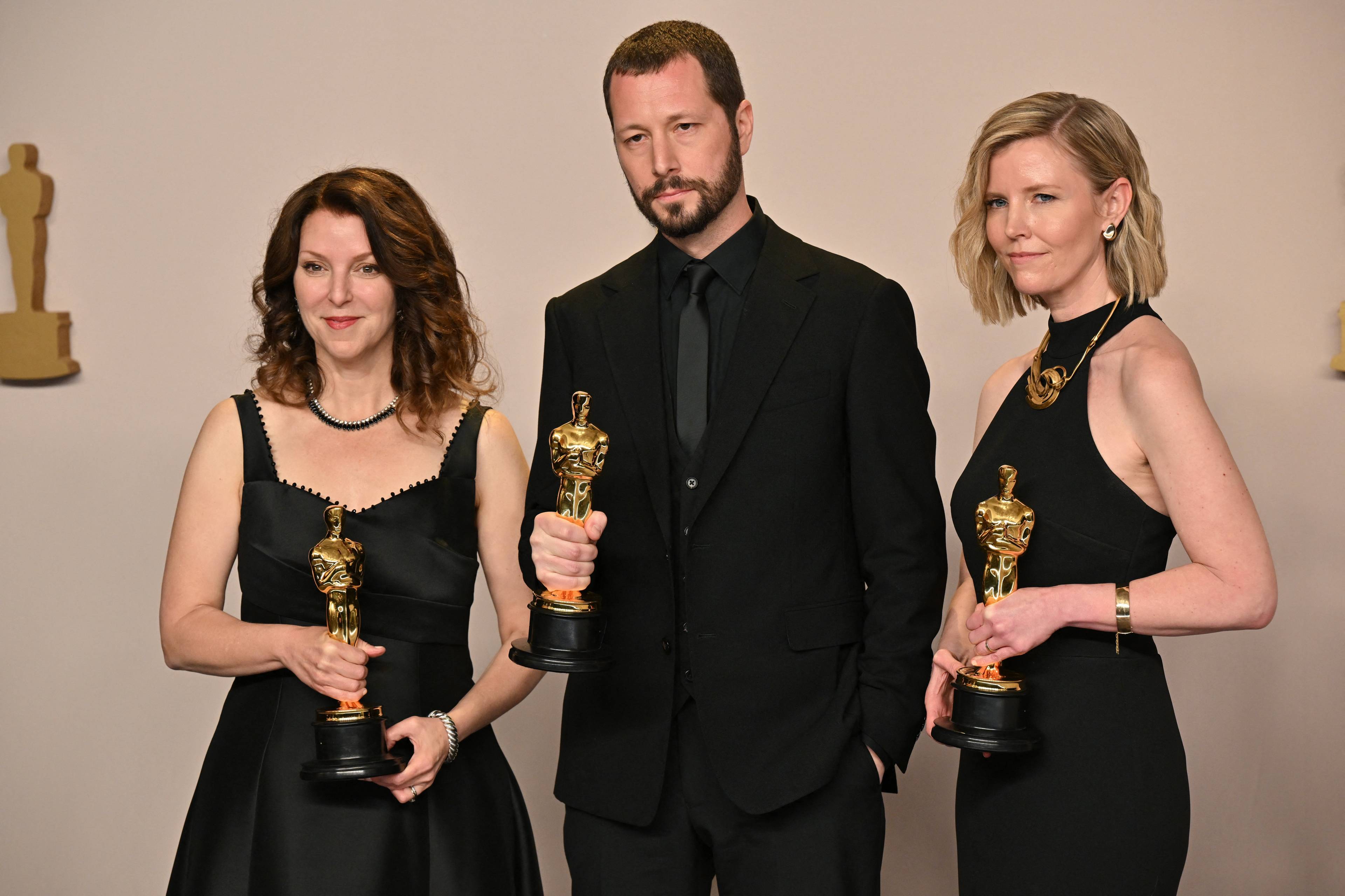 Dwie kobiety i męzczyzna ubrani na czarno trzymają złote statuetki Oscarów