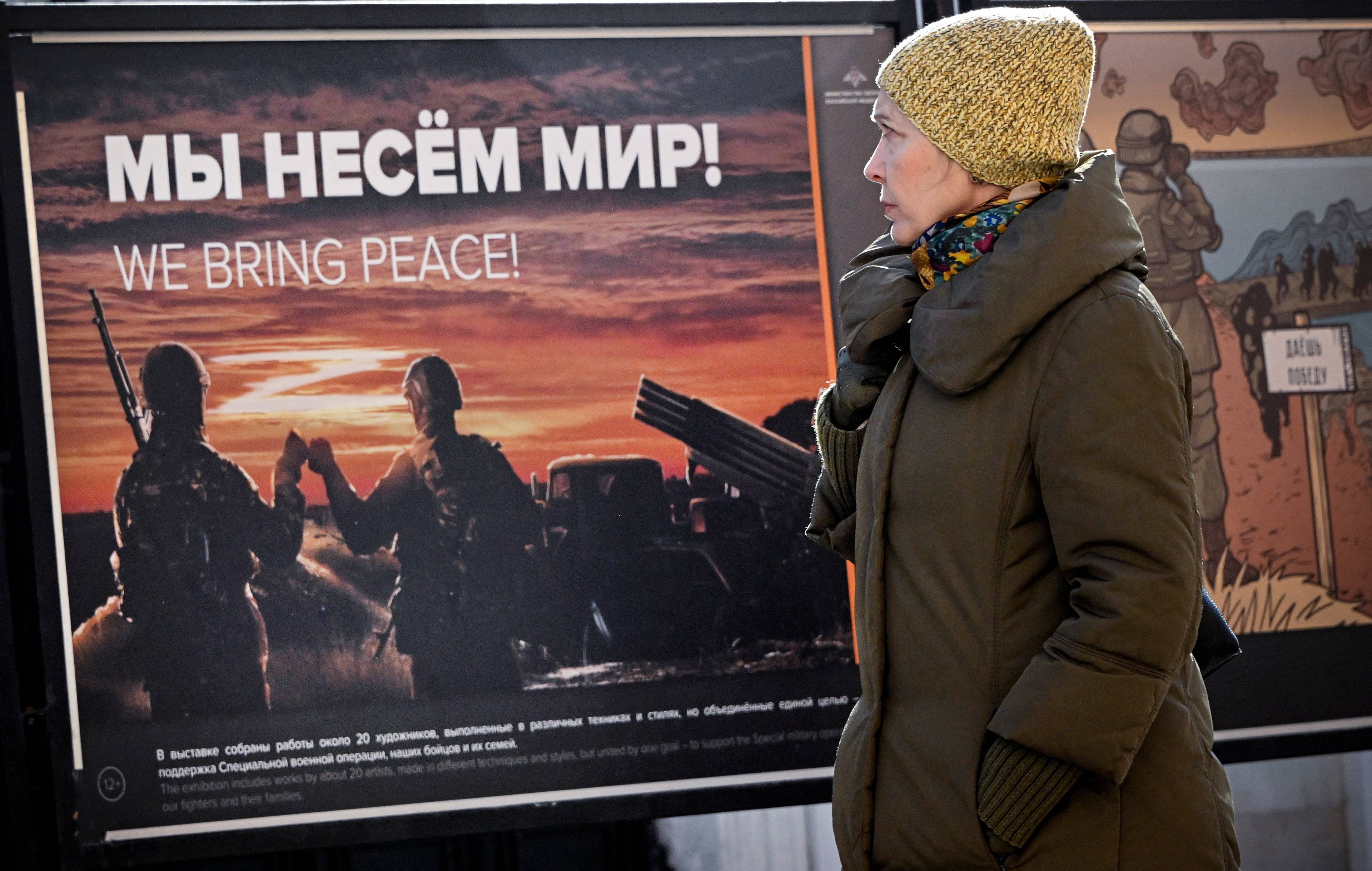kobieta przechodzi przed plakatem z żołnierzami i napisem po rosyjsku „niesiemy pokój"
