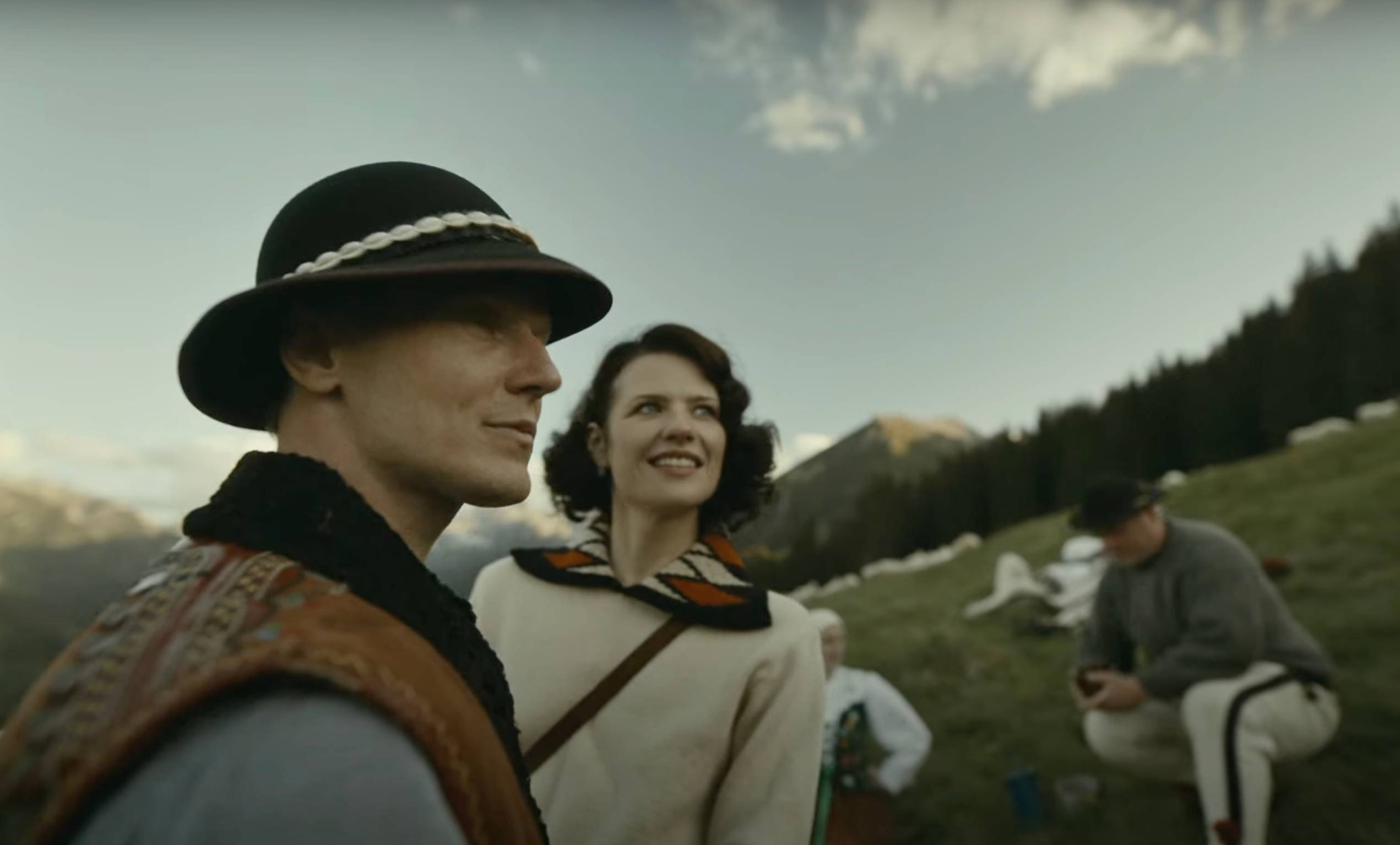 Mężczyzna w góralskim stroju i kobieta stoją na hali w Tatrach. Za nimi widać górala wypasającego owce. Film „Biała odwaga”