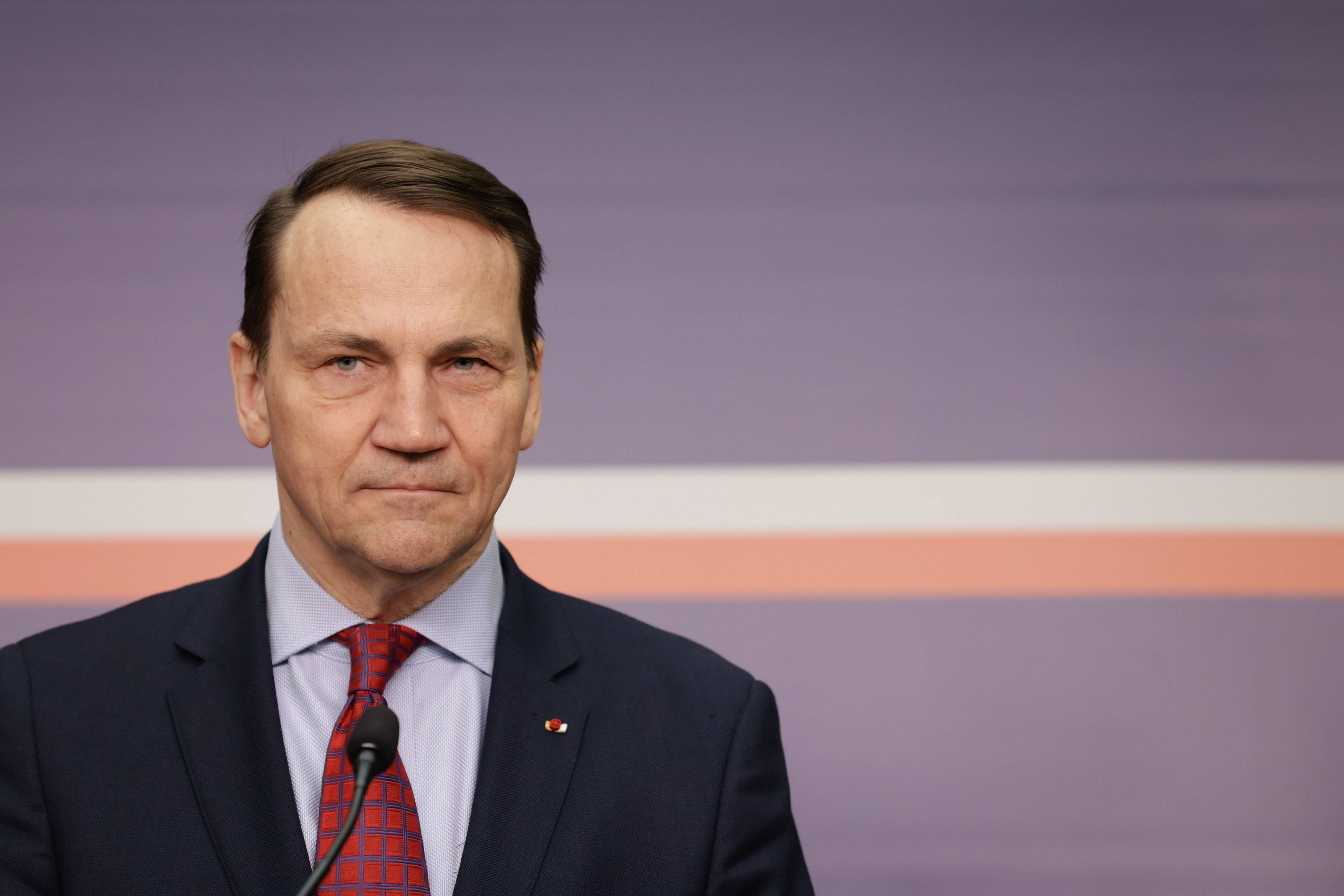 Szef polskiej dyplomacji Radosław Sikorski na tle ciemnoniebieskiej ściany z biało-czerwonym paskiem