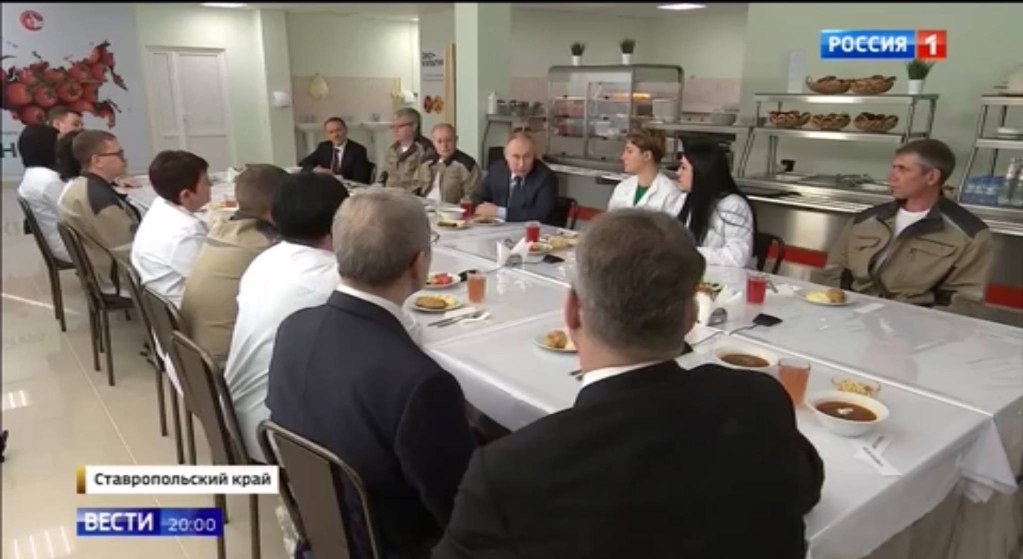 Ludzie w stołówce siedzą przy obiedzie (zupa, drugie, surówka i kompot). W srodku Putin