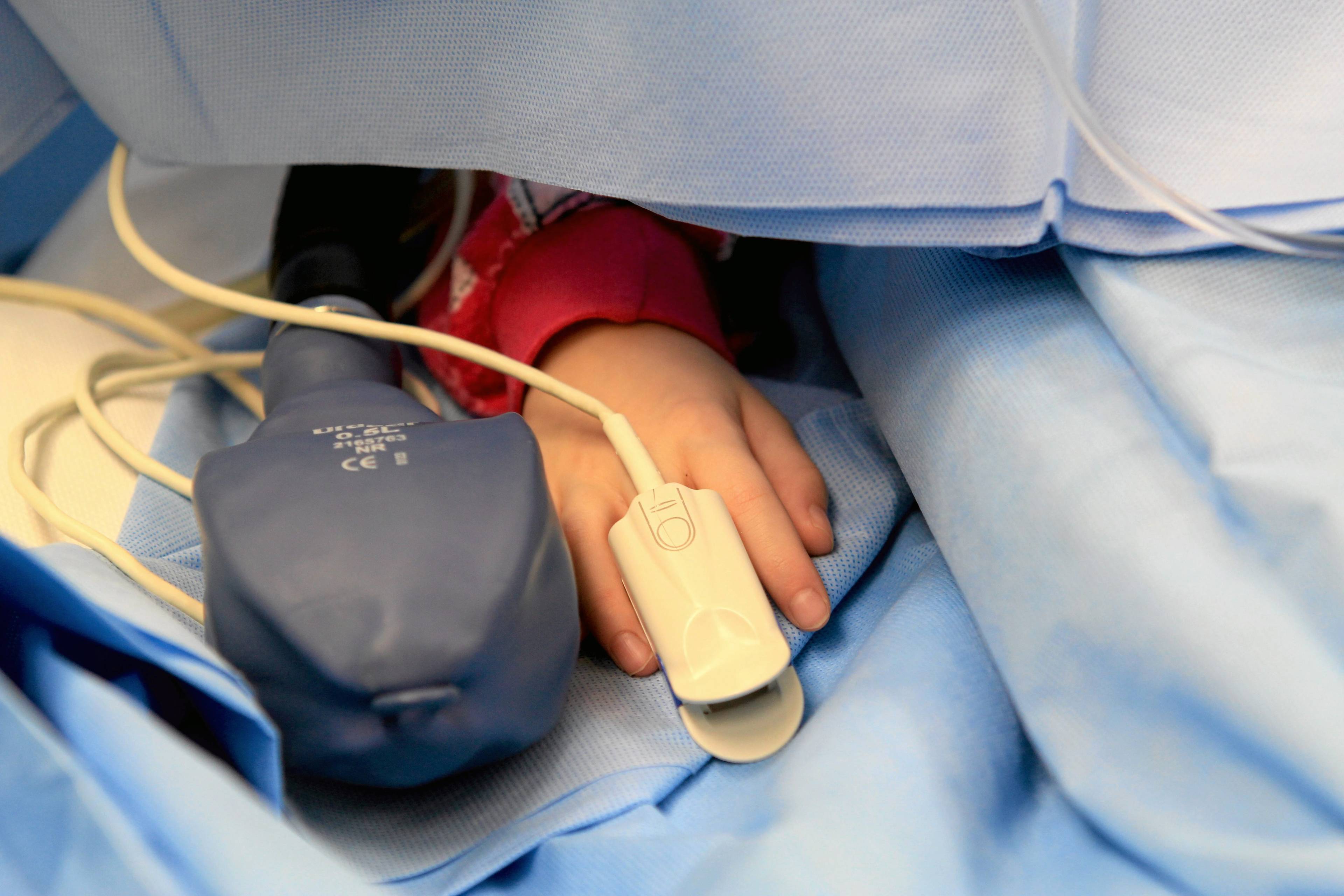 ręka dziecka z pulsometrem na palcu wystaje spod kołdry