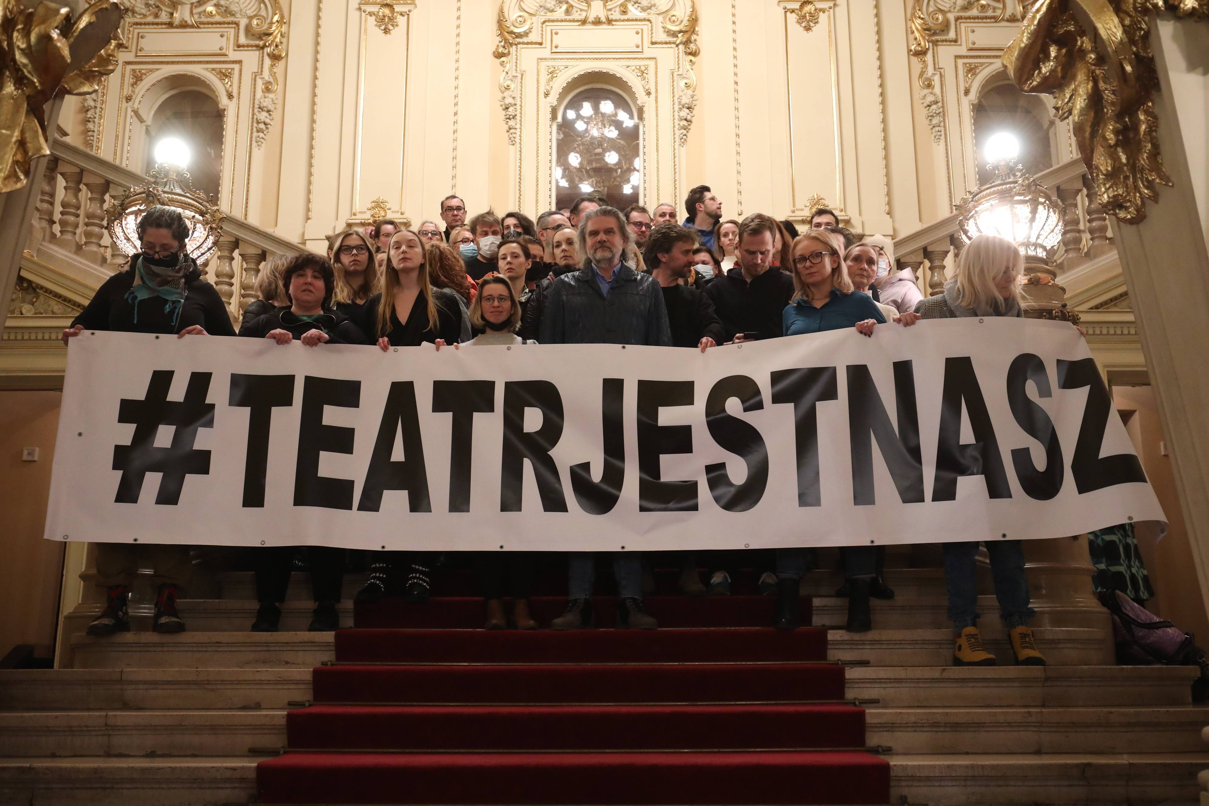 grupa osób stoi na schodach i trzyma napis "Teatr jest nasz"