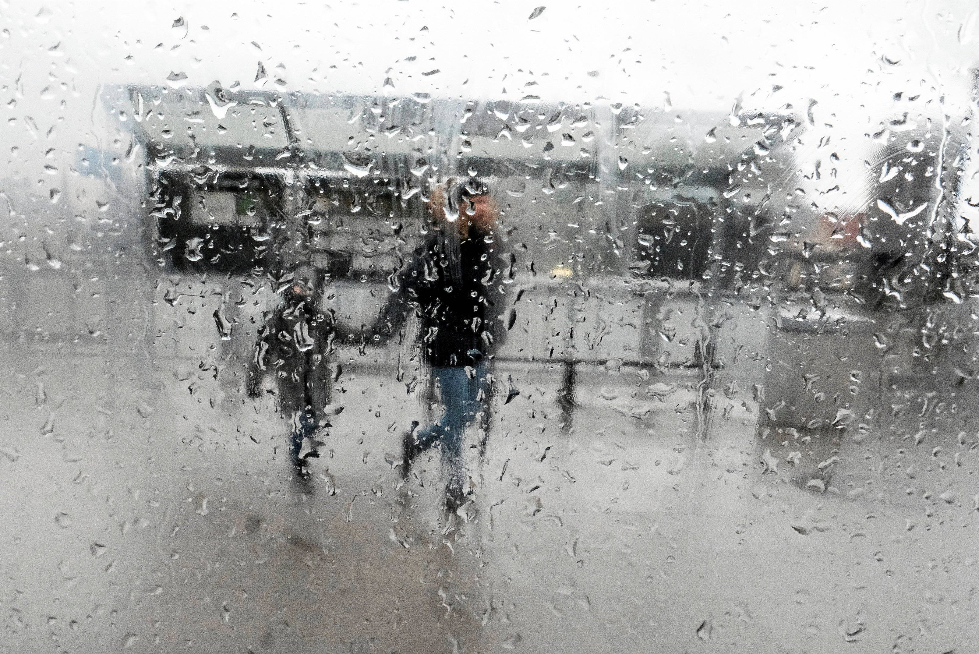 Dwie osoby trzymają się za ręce za szybą w deszczu