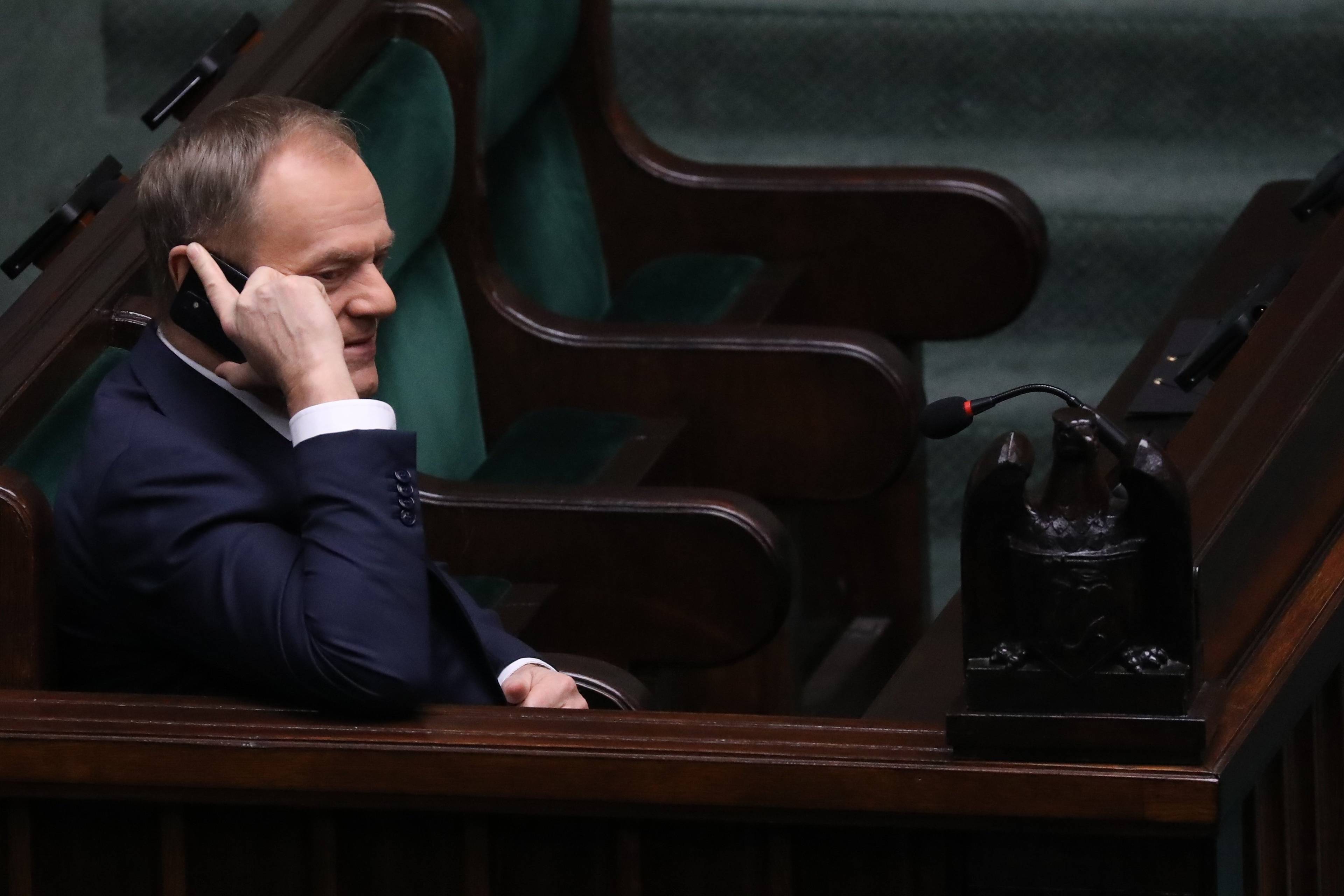 Mężczyzna w ławach rządowych w Sejmie, trzyma telefon komórkowy przy uchu. Donald Tusk, sondaż Ipsos