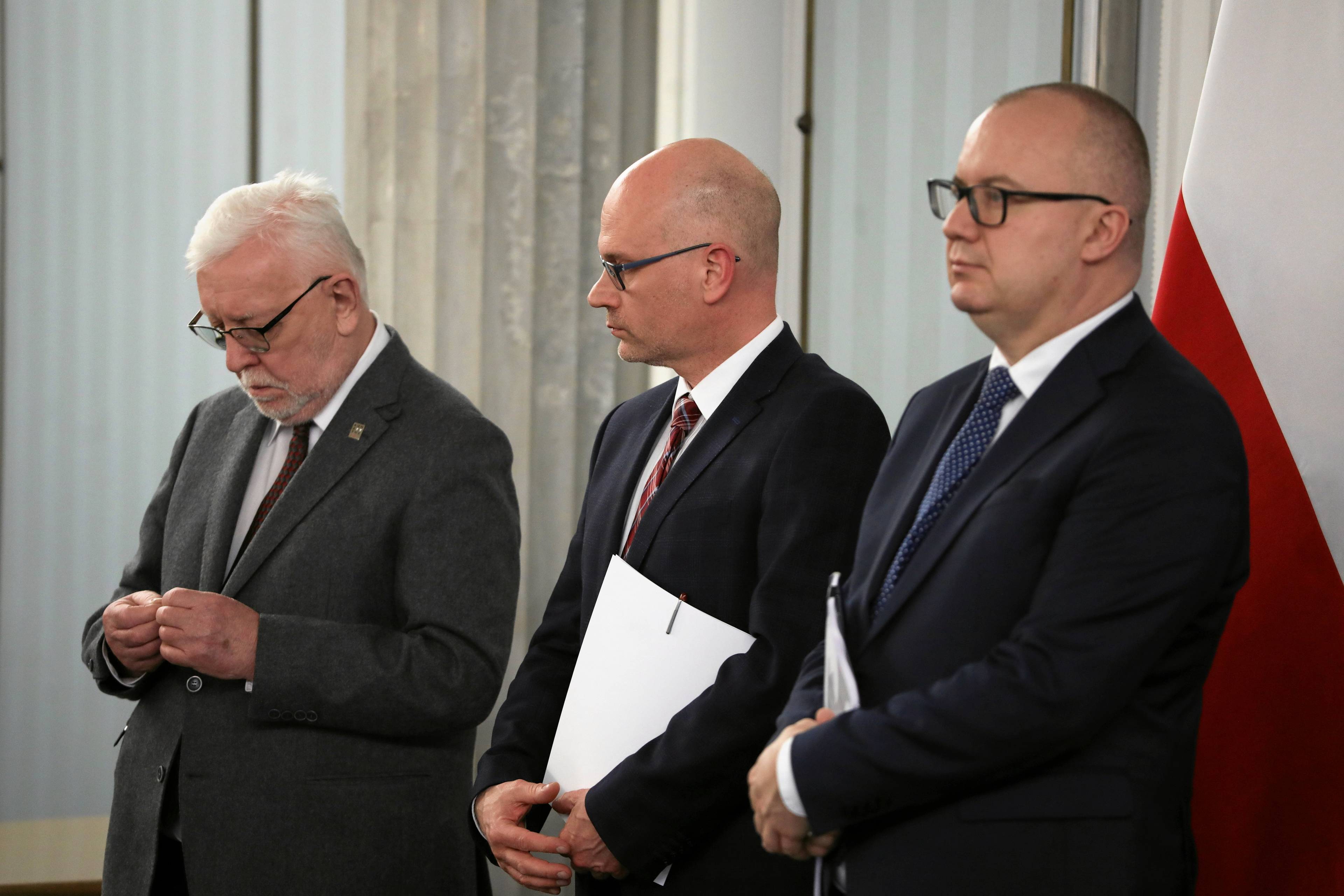 Trzech mężczyzn z krótkimi włosami w garniturach stoi podczas konferencji prasowej w Sejmie