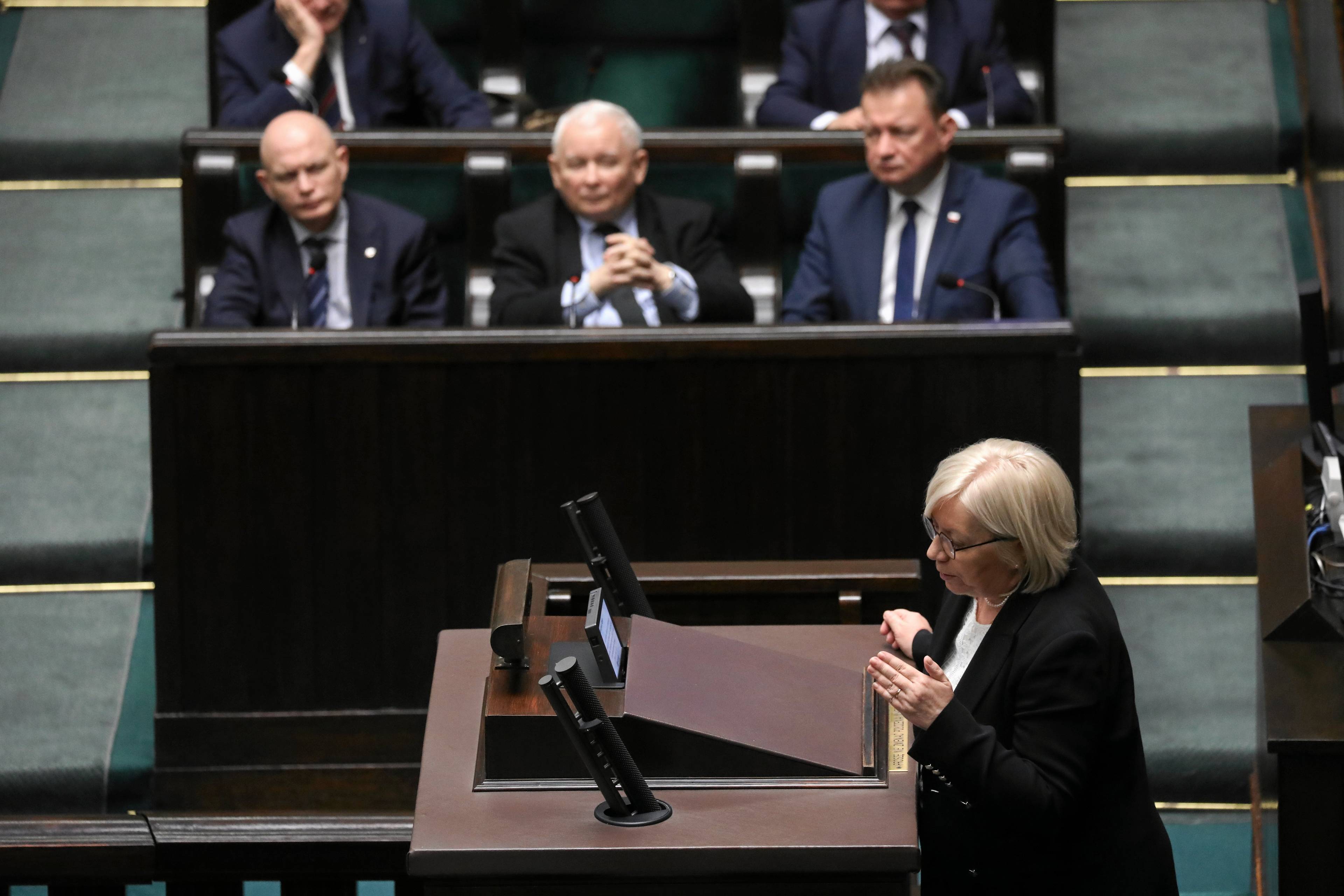 Na zdjęciu widzimy Julię Przyłębską, prezes TK, która przemawia w Sejmie. W tle w ławach siedzą Jarosław Kaczyński, Mariusz Błaszczak i Waldemar Andzel.