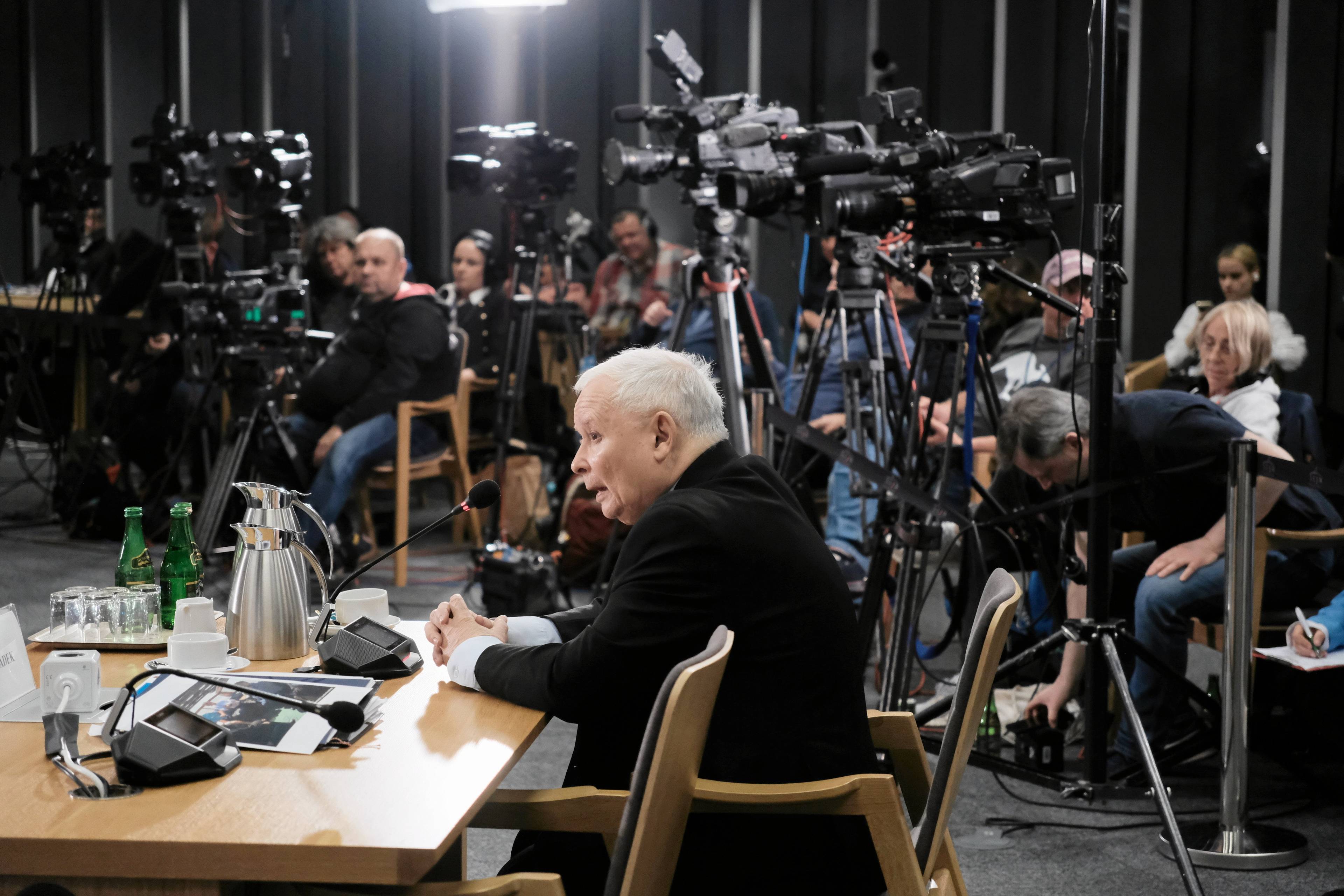 Kaczyński siedzi na krześle, za nim fotoreporterzy