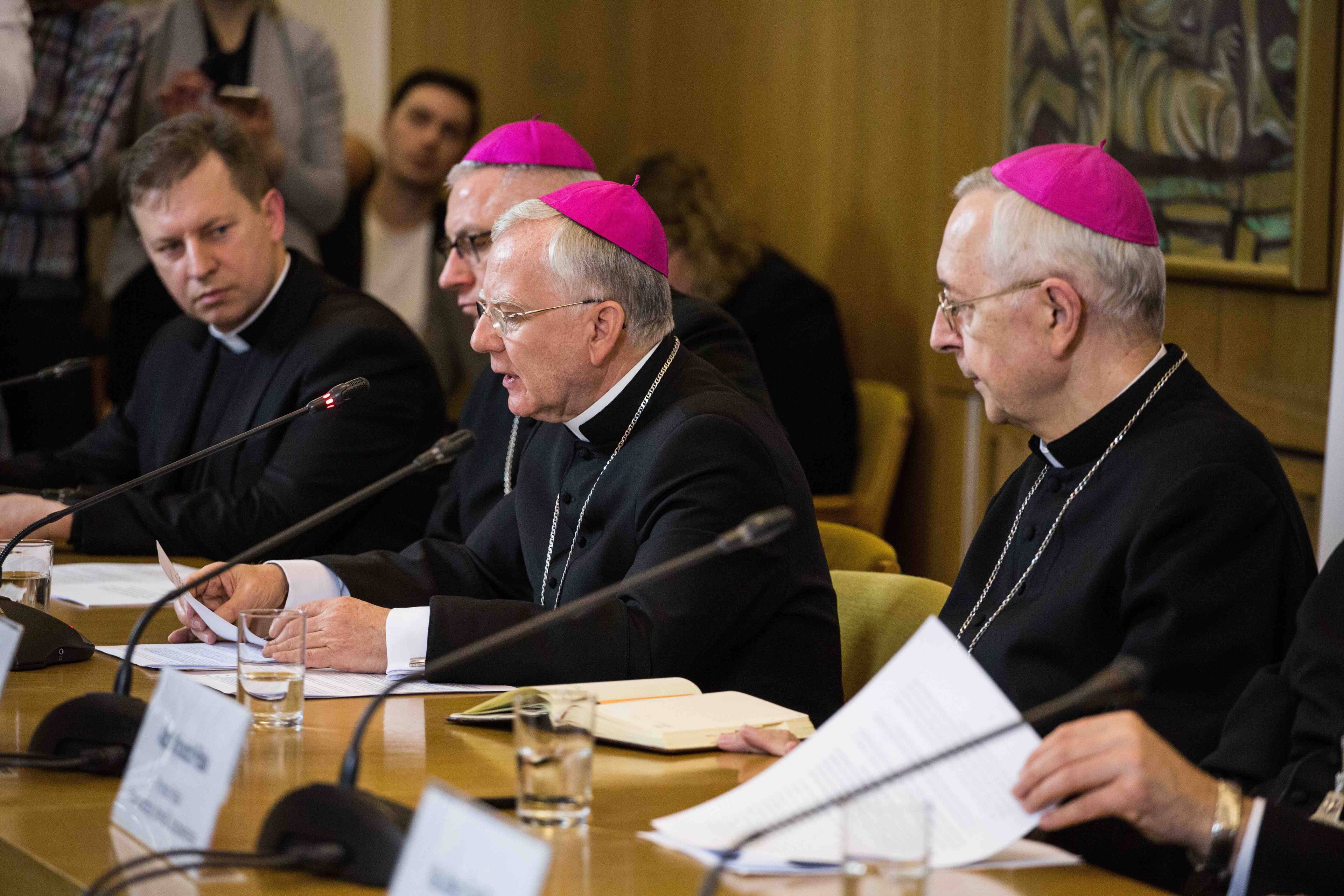 Trzech biskupów siedzi przy stole podczas konferencji prasowej. Episkopat