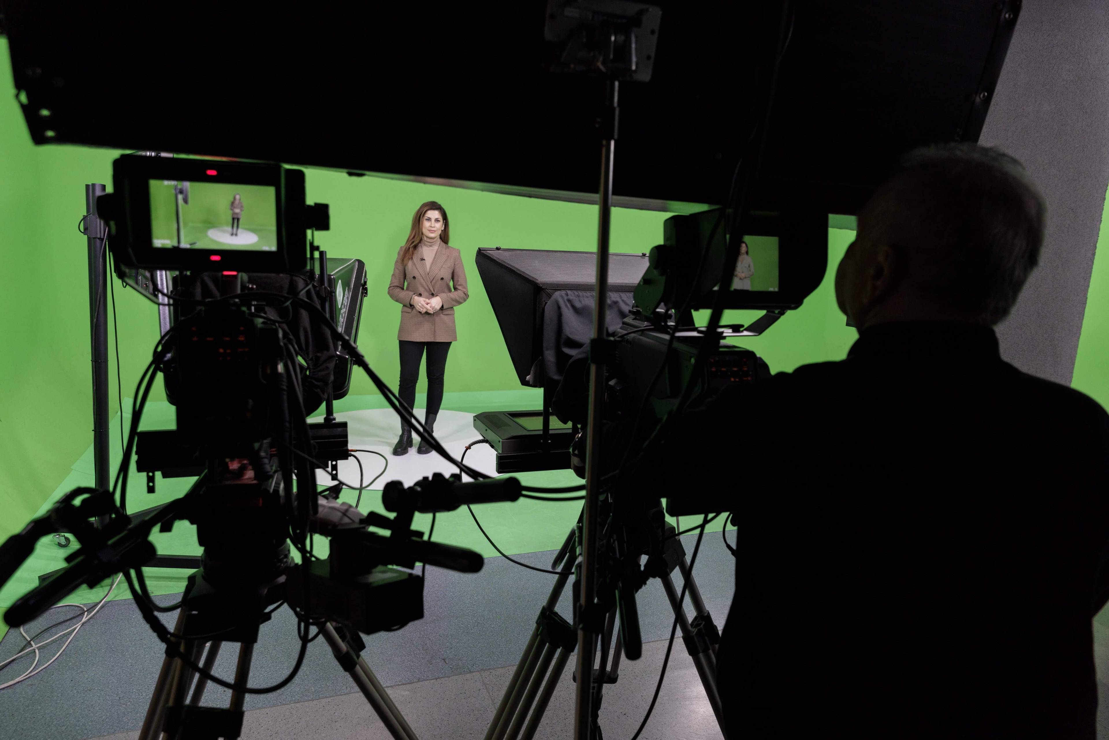 Kobieta stoi przed kamerami na tle green boxu w studiu telewizyjnym.