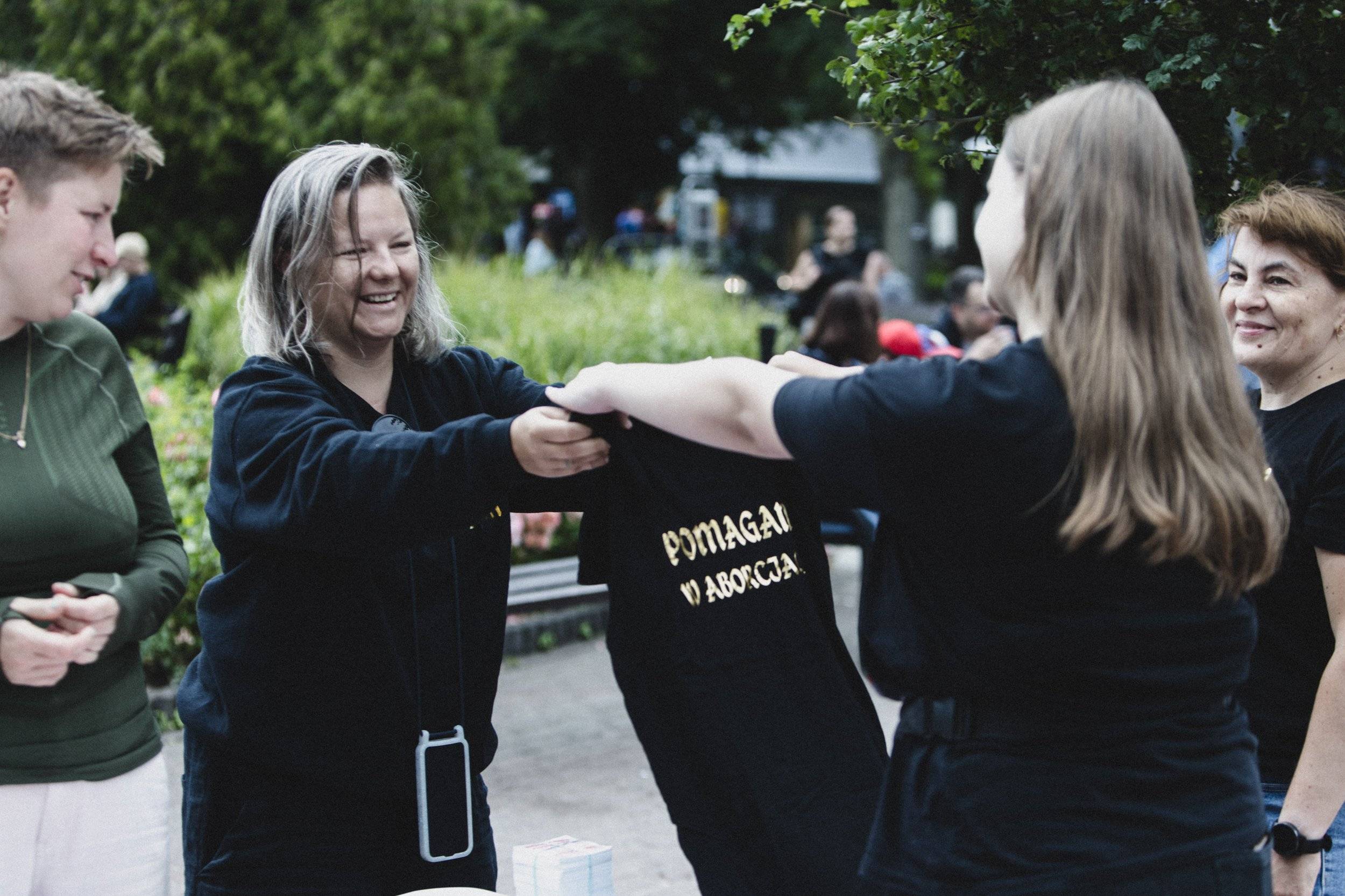 Dwie kobiety trzymają czarny tiszert z napisem „Pomagam w aborcji”