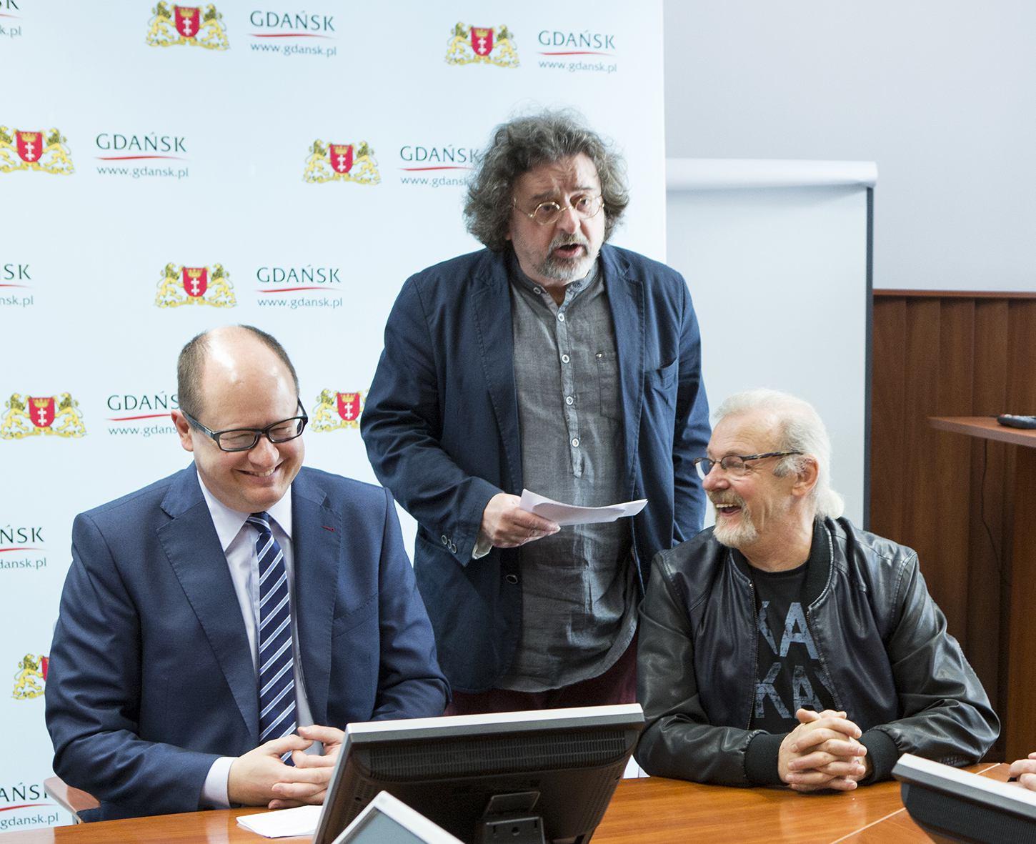 Paweł Adamowicz siedxzi uśmiechnięty, obok stoi jego ówczesny rzecznik Antoni Pawlak