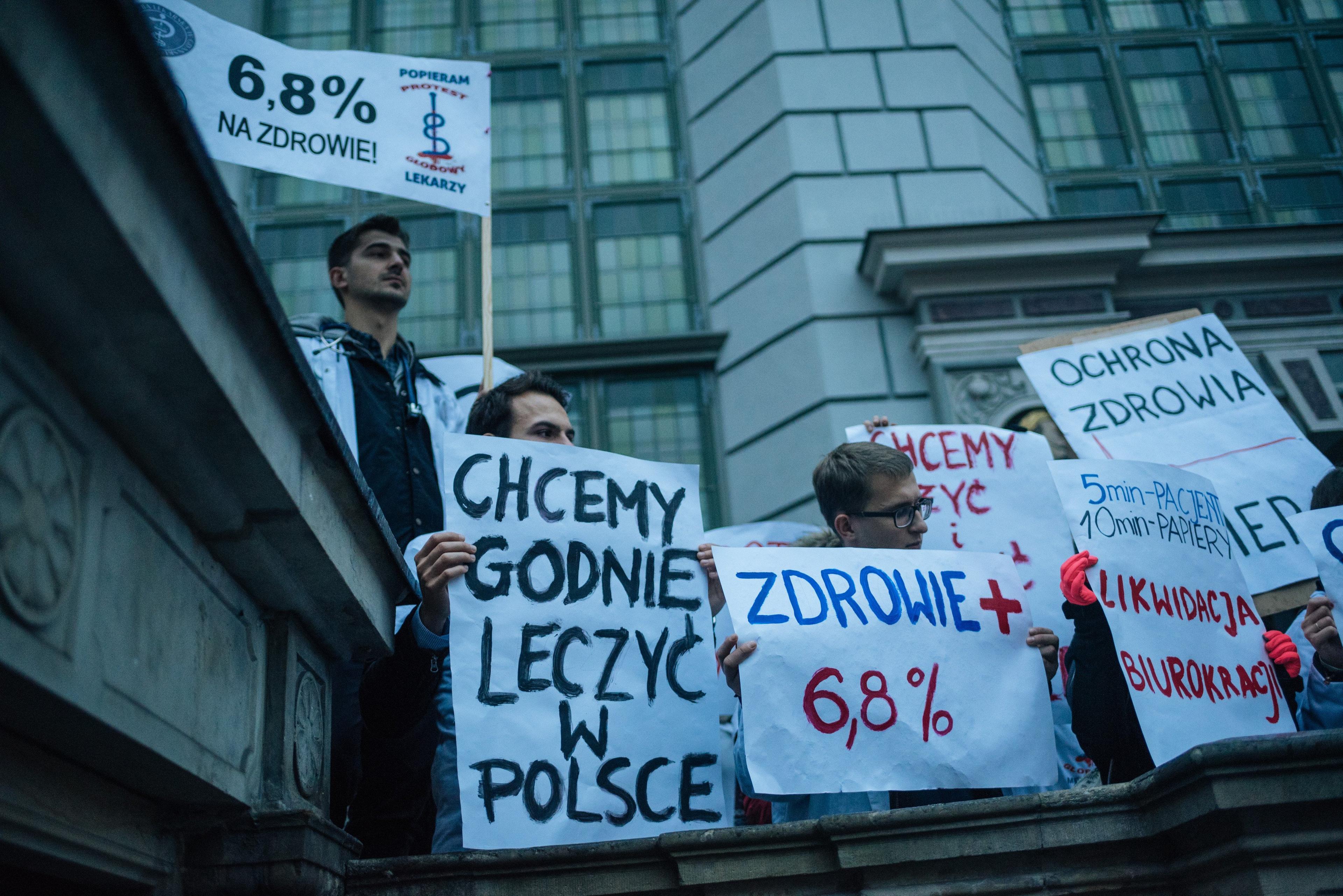 Lekarze rezydenci trzymają plakat z napisem"Chcemy godnie leczyć w Polsce"