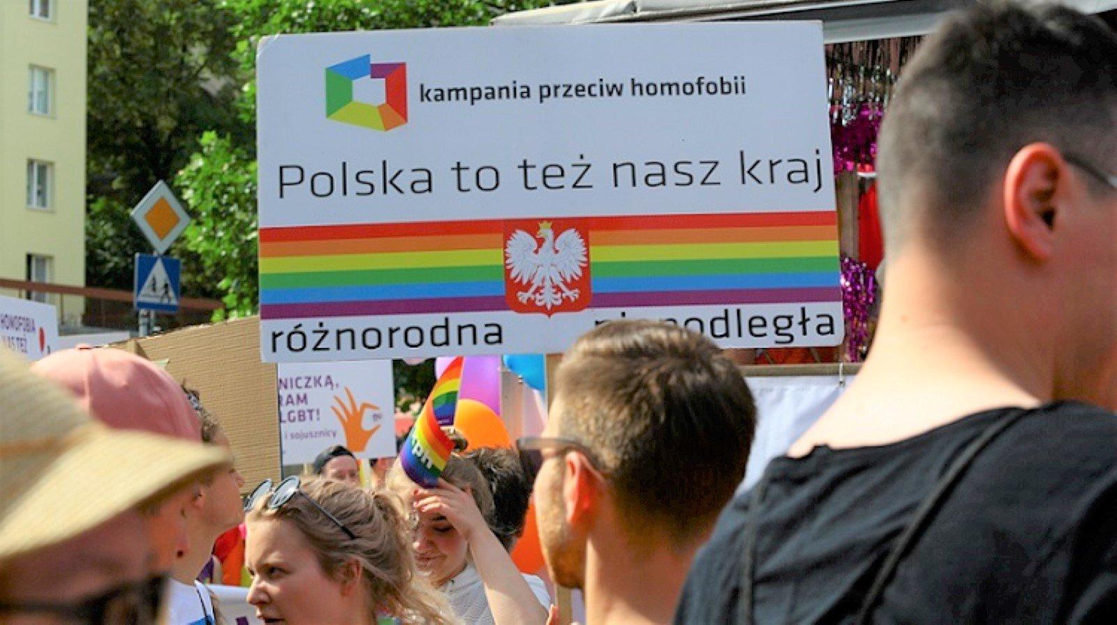 Młodzi ludzie na tle baneru "Polska to też nasz kraj" z kolorami tęczy