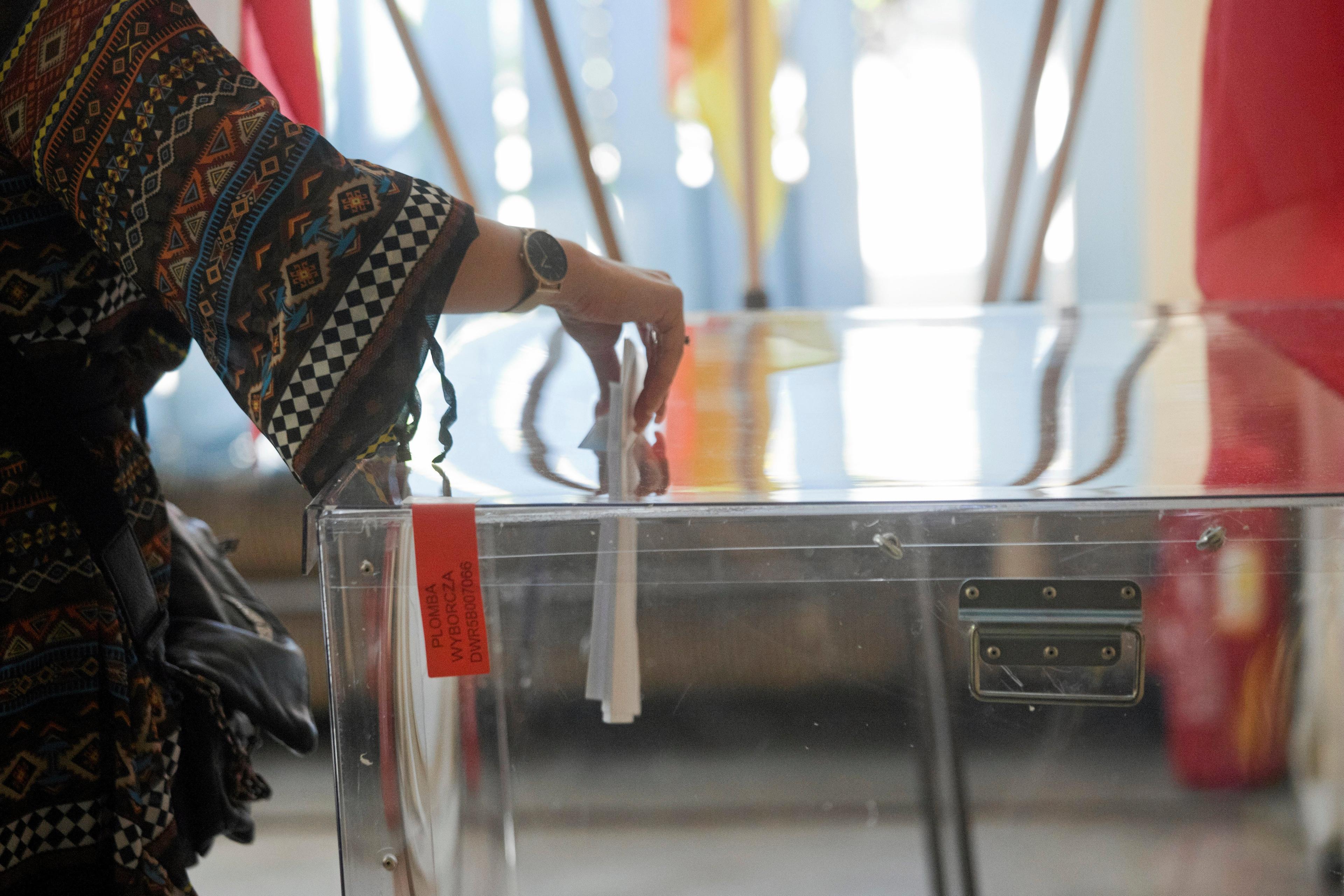 ręka wrzucająca kartę do głosowania do przezroczystej urny